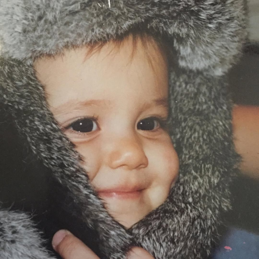 Ariana Grande as a toddler, wrapped in a soft, furry hood. Her dimpled smile and wide eyes full of warmth and early spark | Source: Instagram/arianagrande
