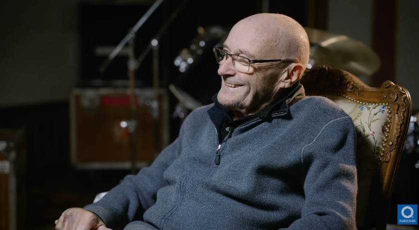 Phil Collins is seen smiling during a sit-down video interview dated January 7, 2025, where he looked back on the highlights of his storied career. The moment captured shows a rare glimpse of levity as Collins spoke about the past with warmth, humour, and reflection despite the physical challenges he continues to face. | Source: YouTube/Drumeo