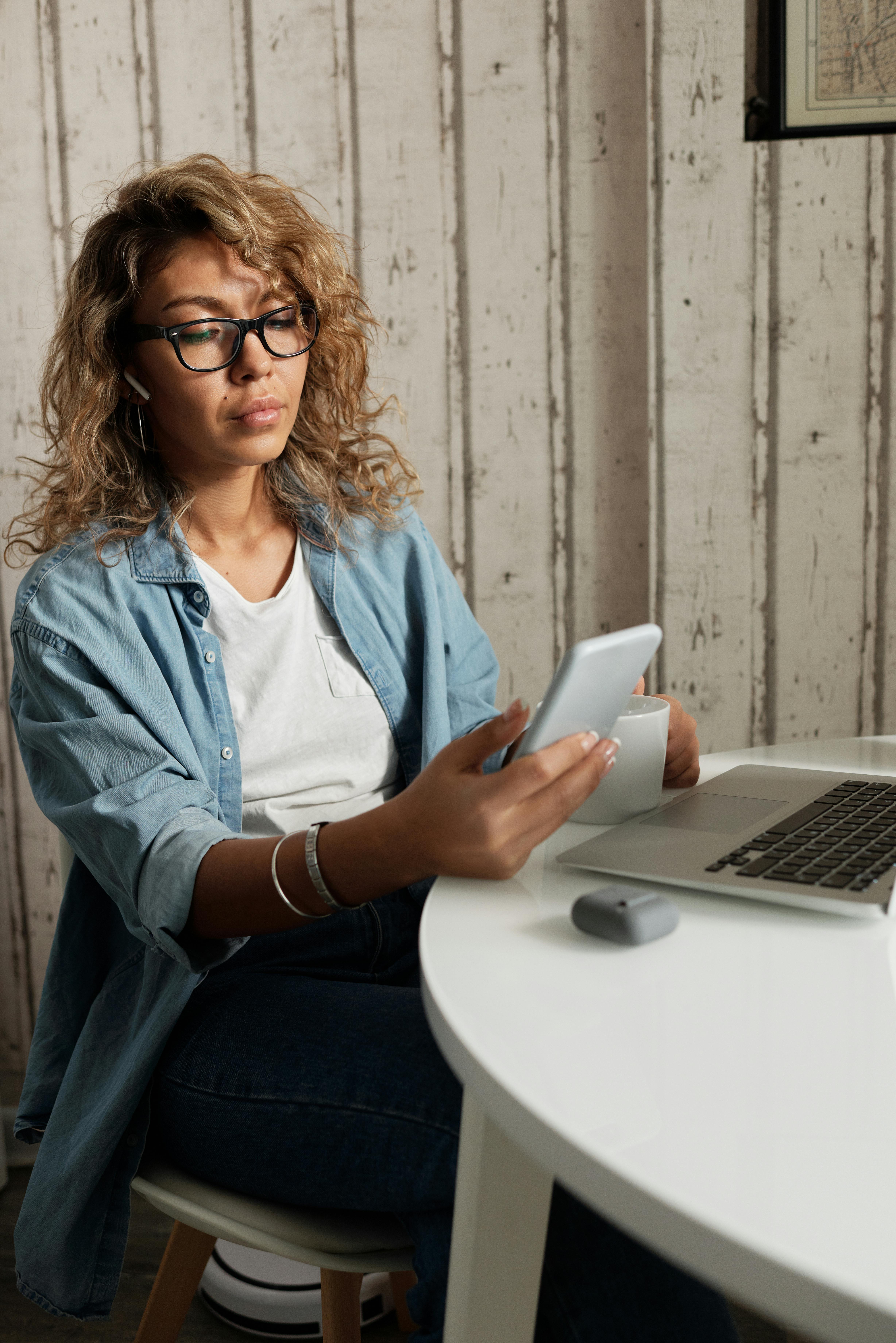 A woman looking at her phone while working on her laptop| Source: Pexels