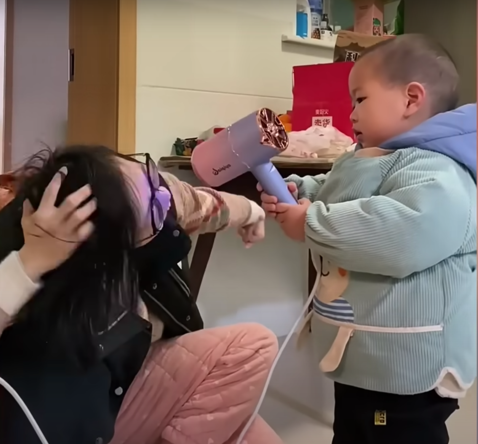 Pomelo ayuda a su madre a sujetar el secador de pelo. | Foto: Youtube.com/South China Morning Post
