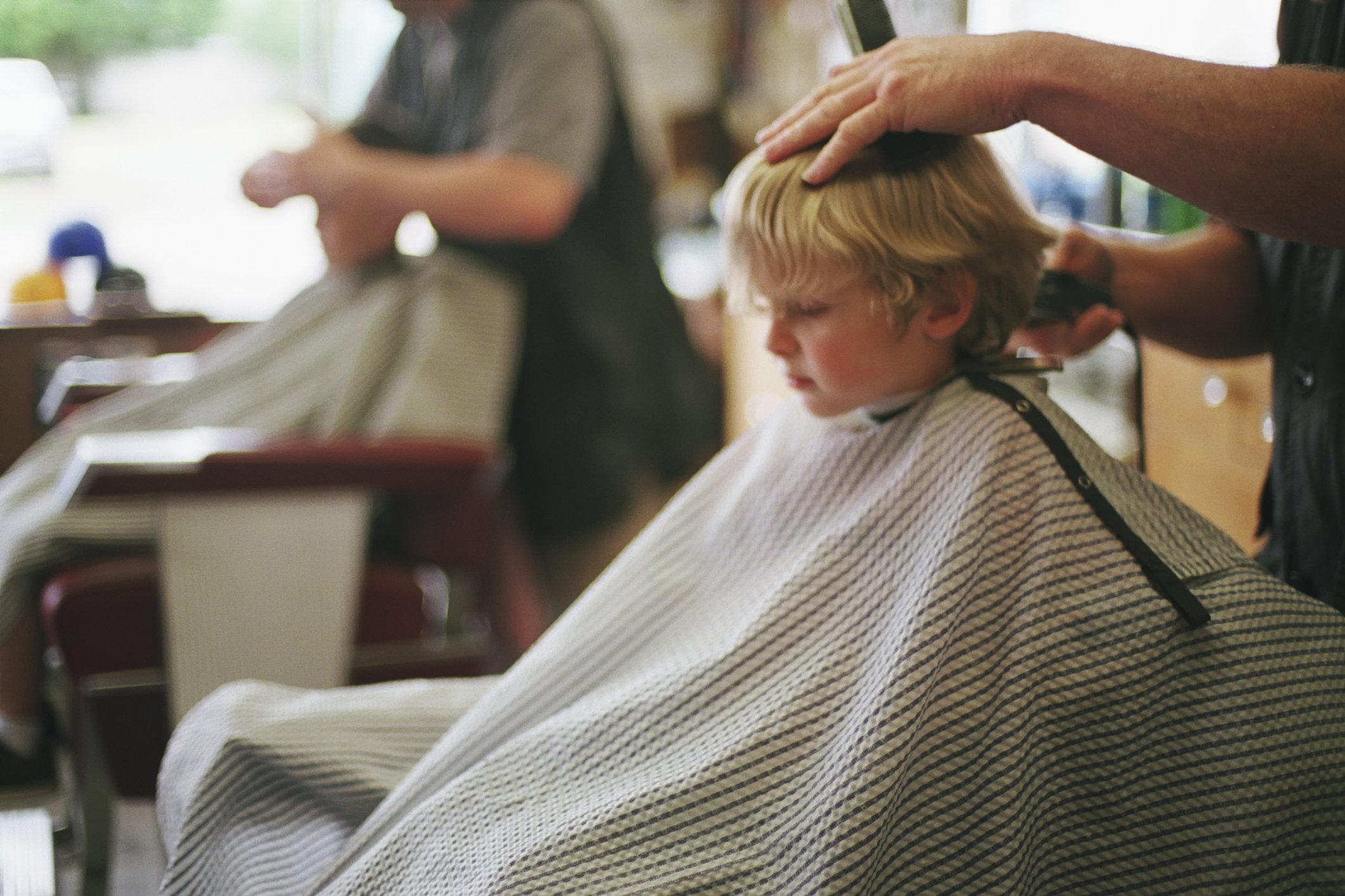 A young, five-year-old boy sits patiently while getting his hair cut at a local barbershop. | Photo: Getty Images