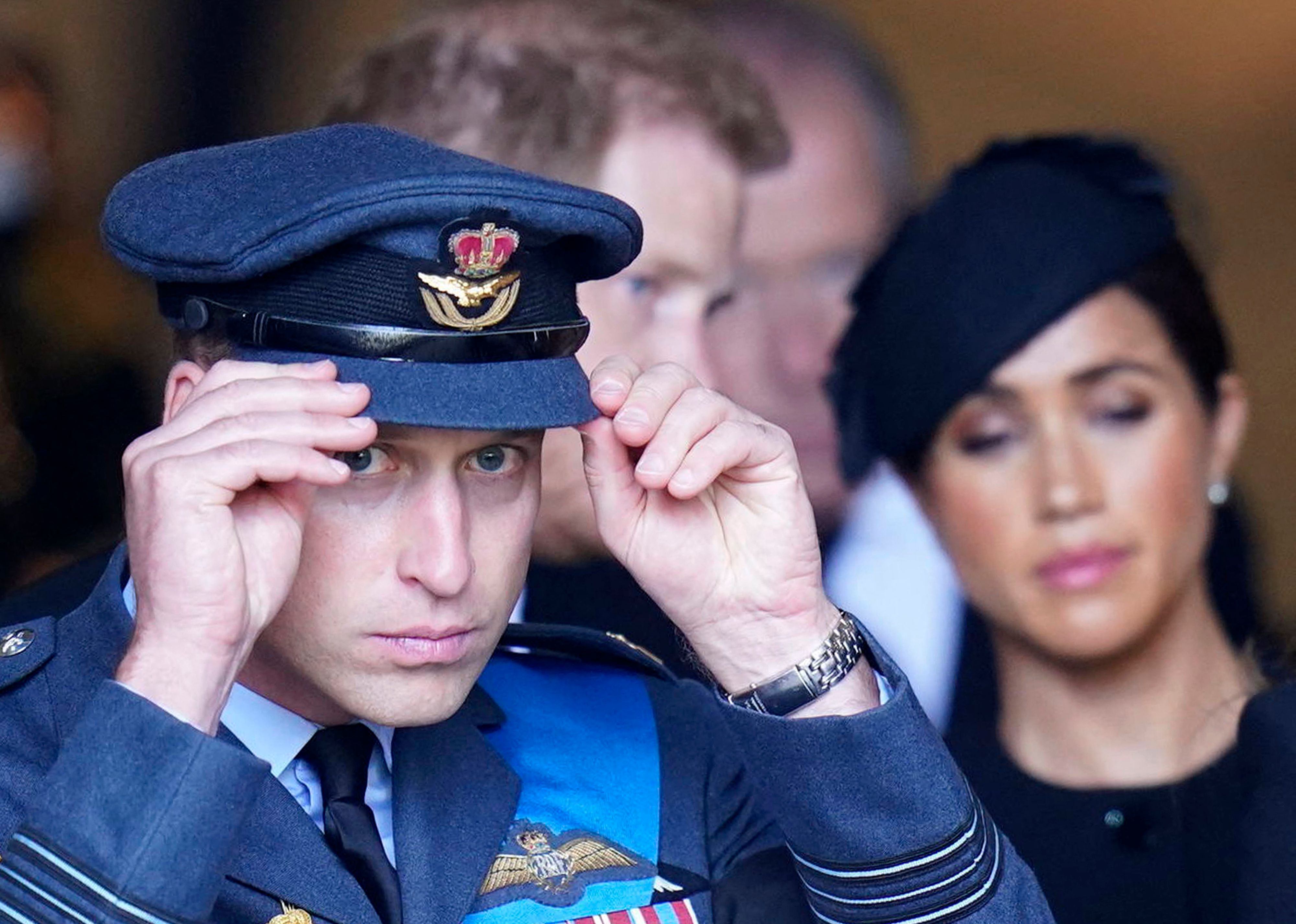 Prince Harry adjusts his cap and walks ahead of Prince William and Meghan Markle at Westminster Hall in London on September 14, 2022 | Source: Getty Images