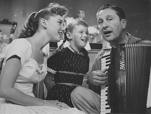 US musician and band leader, Lawrence Welk,playing the accordion with sisters Dianne Lennon (left) and Janet Lennon, both of the 'Lennon Sisters', singing beside him, circa 1955 | Source: Getty Images