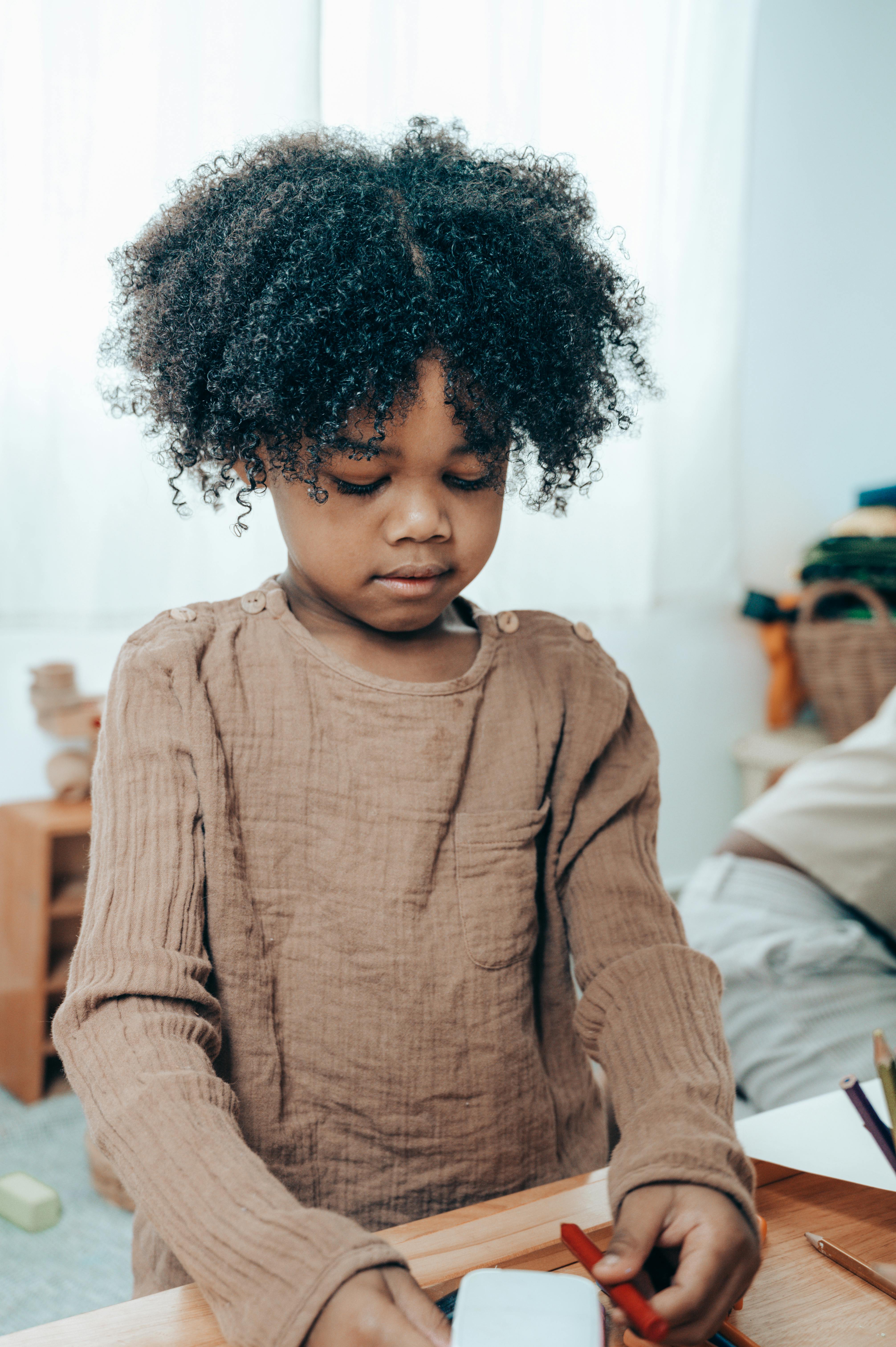 A little girl looking down at a paper and crayon | Source: Pexels