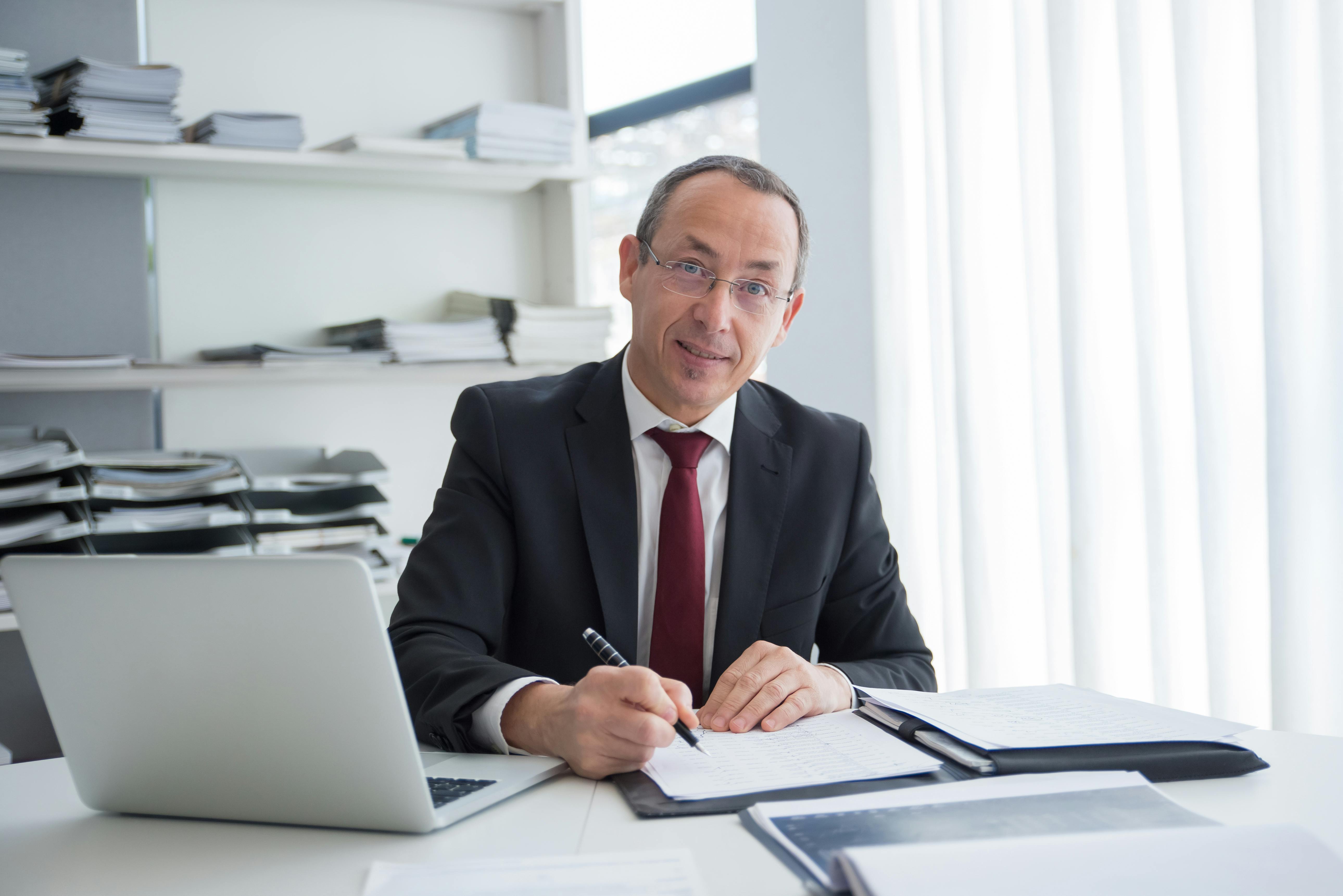 A smiling man sitting with a laptop and some documents | Source: Pexels