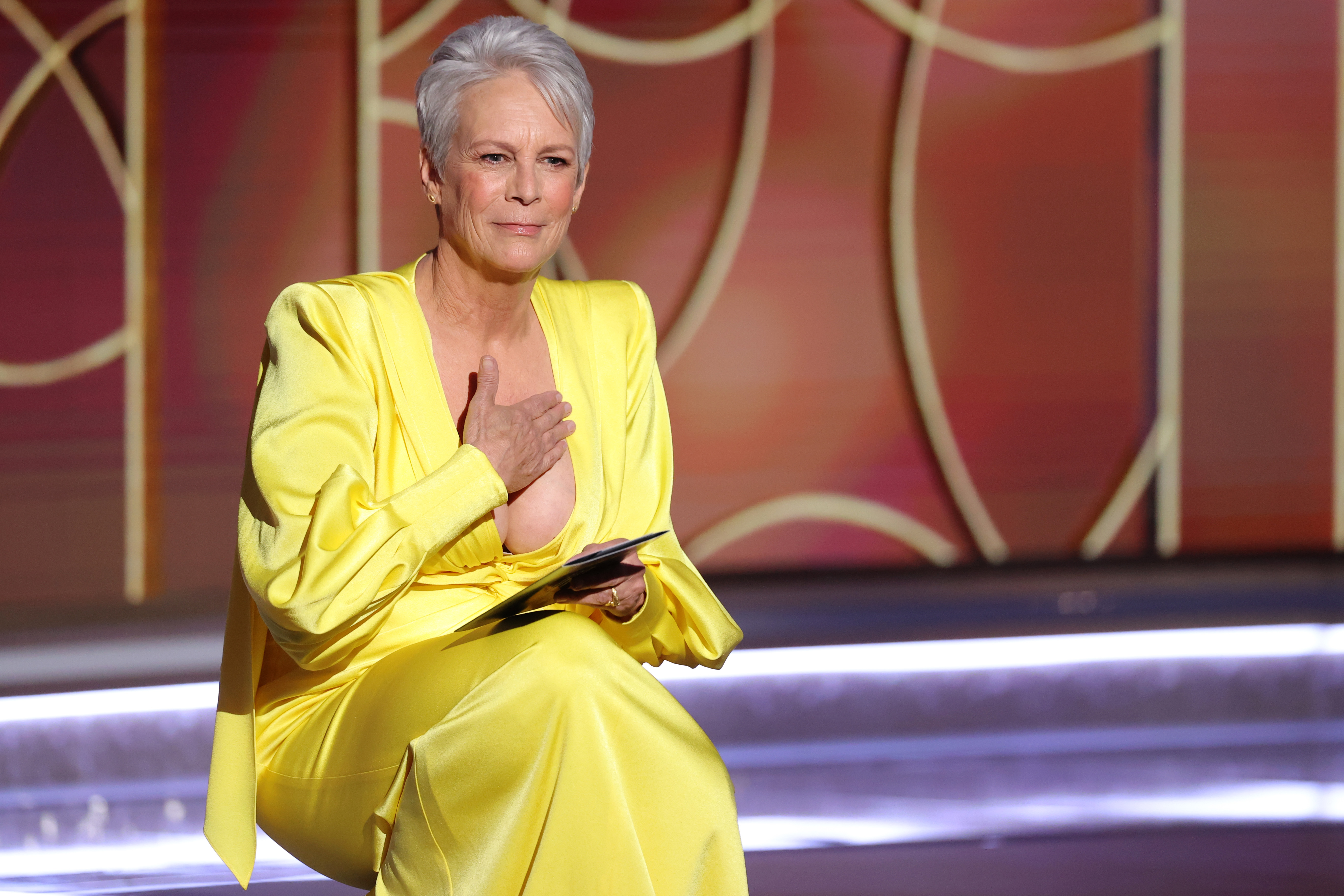 Jamie Lee Curtis takes the stage at the 78th Annual Golden Globe Awards in a radiant yellow satin gown, her silver hair softly swept back as she delivers a heartfelt message under the spotlight.