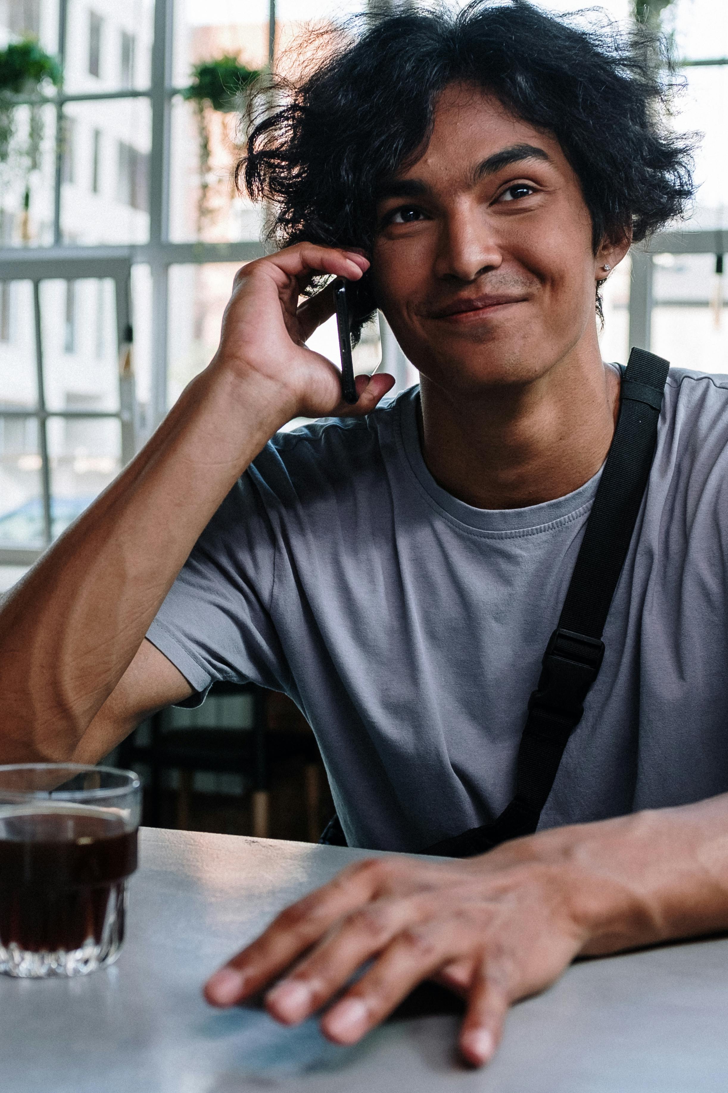 A happy man talking on the phone while having a drink | Source: Pexels