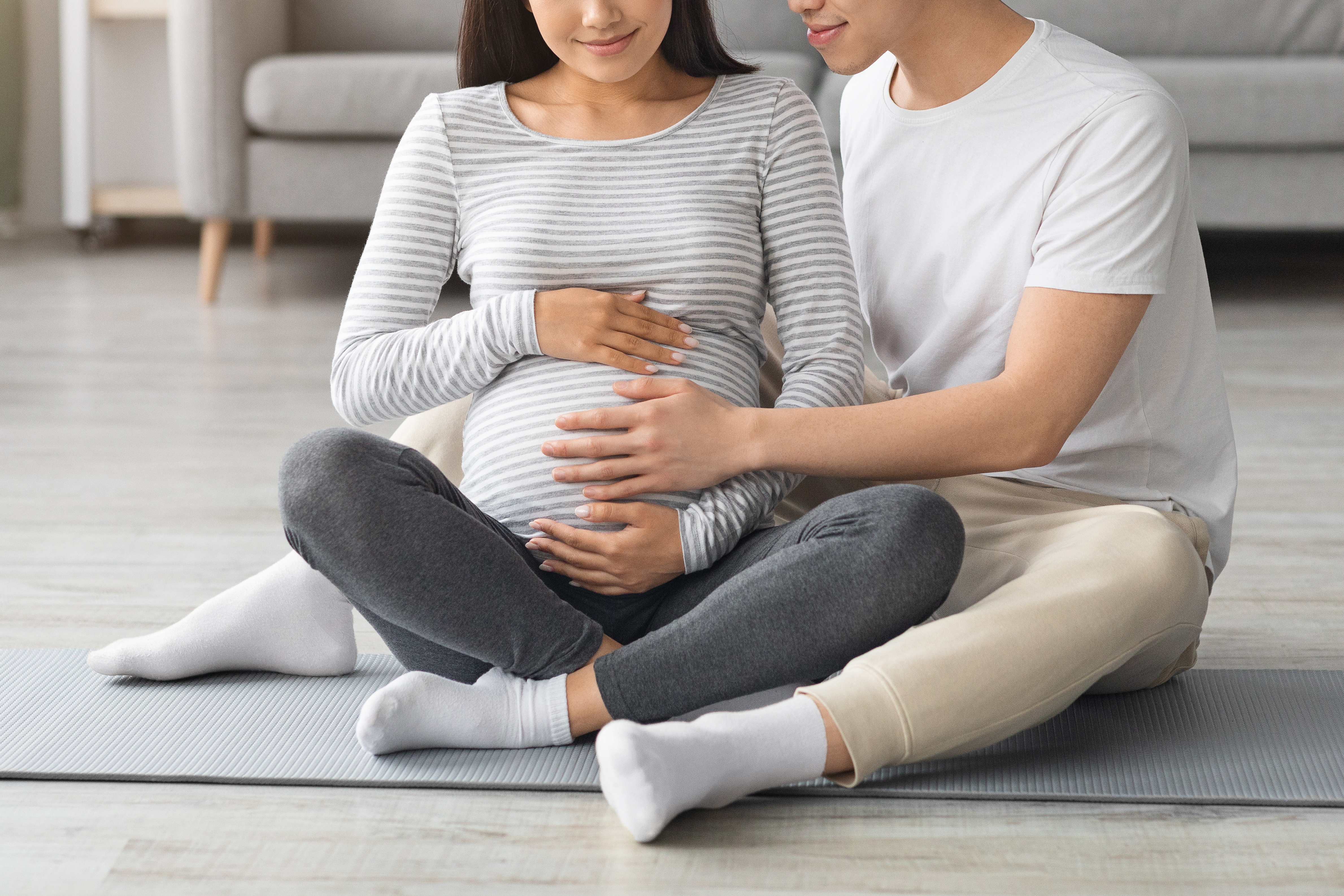 An expecting couple sitting on the floor while cradling the woman's baby bump | Source: Shutterstock