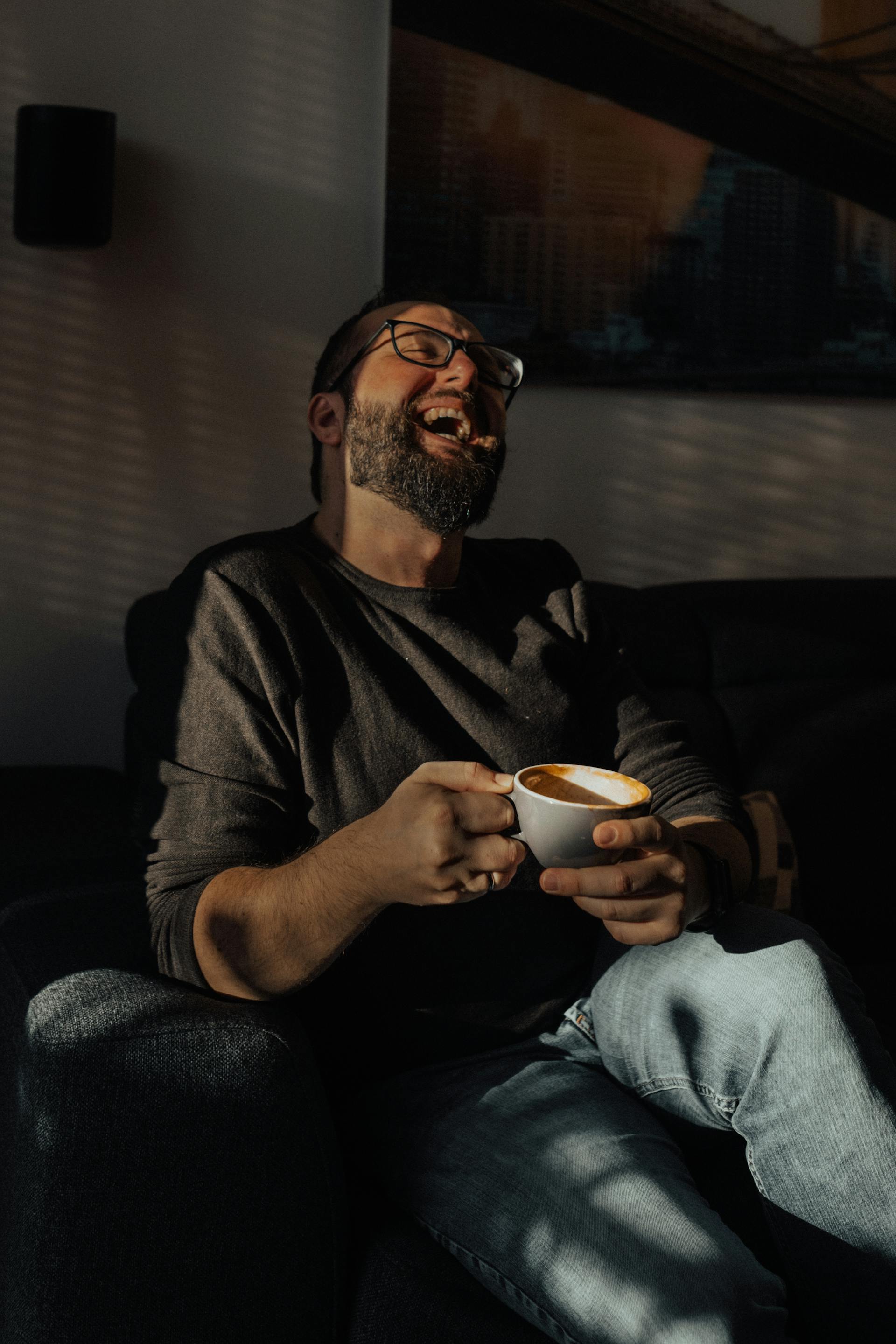A man laughing while holding a cup of coffee | Source: Pexels