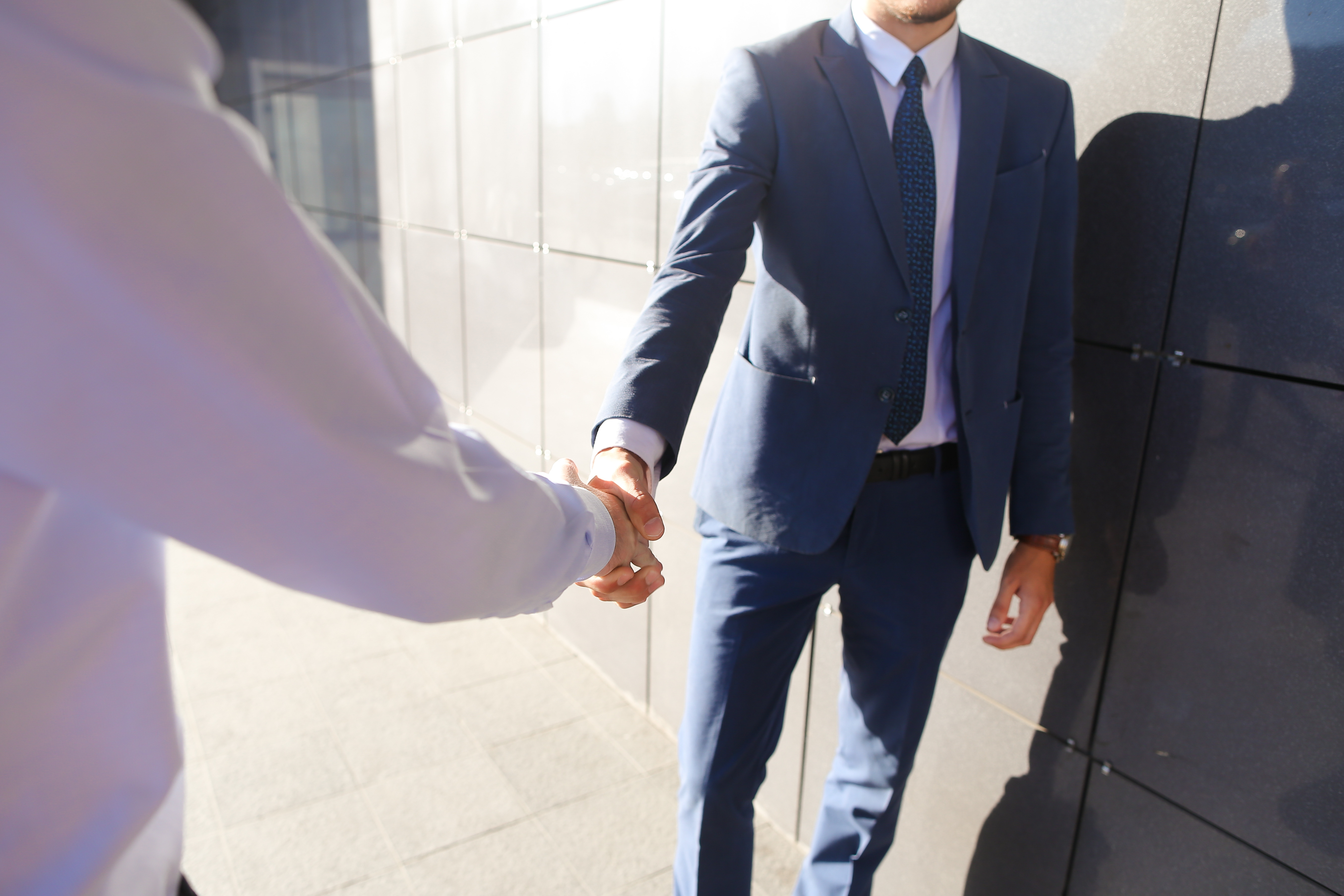 Friends met and greet each other with handshake near gray wall of business center outdoors. | Source: Shutterstock