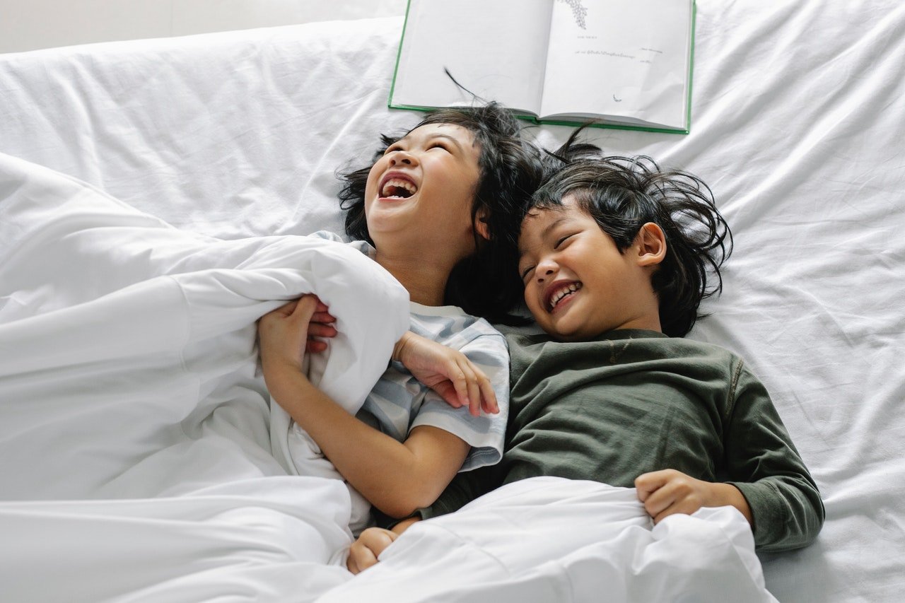 Two kids smiling while lying on the bed | Photo: Pexels
