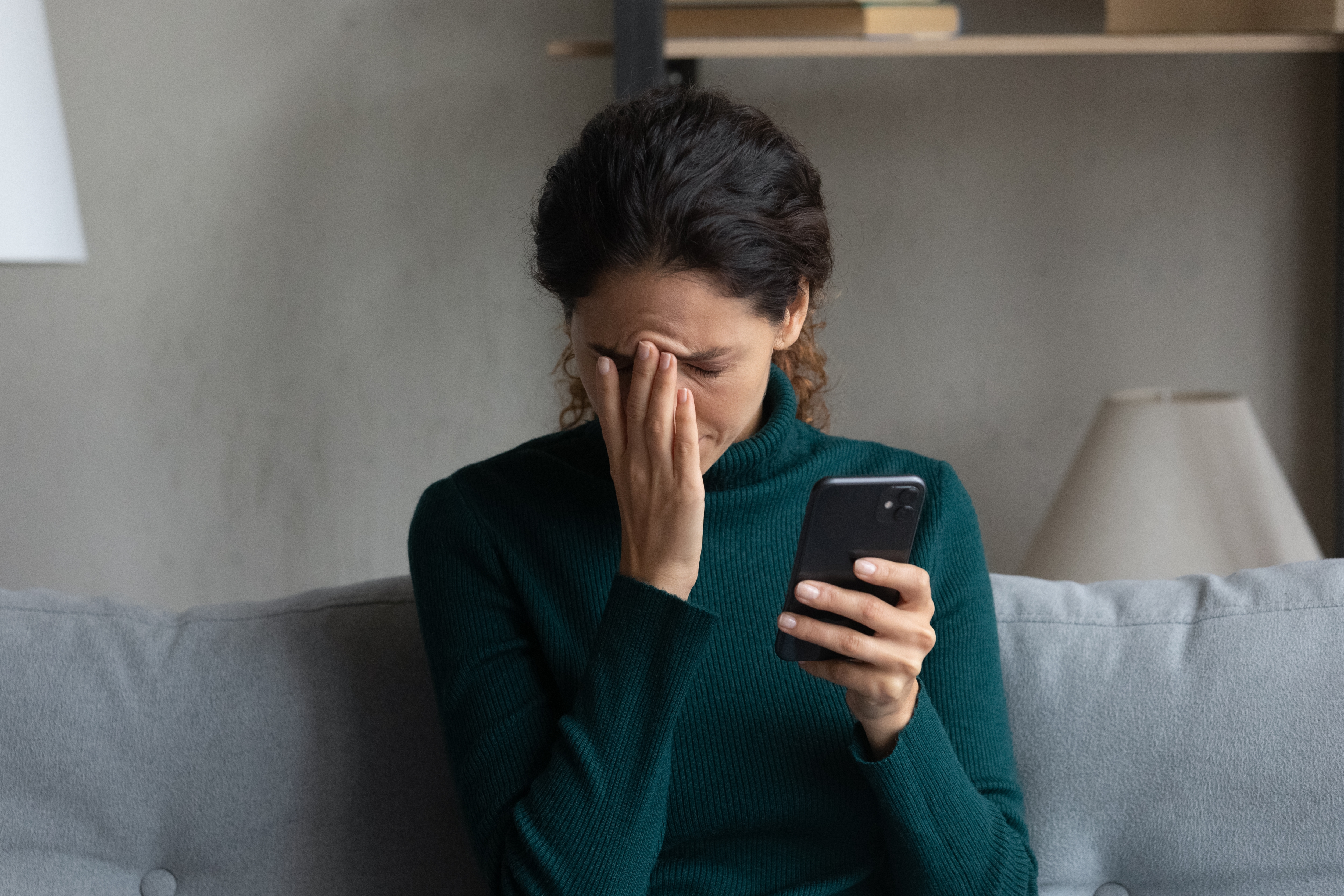 A woman with her head in her hand as she looks at her phone | Source: Shutterstock