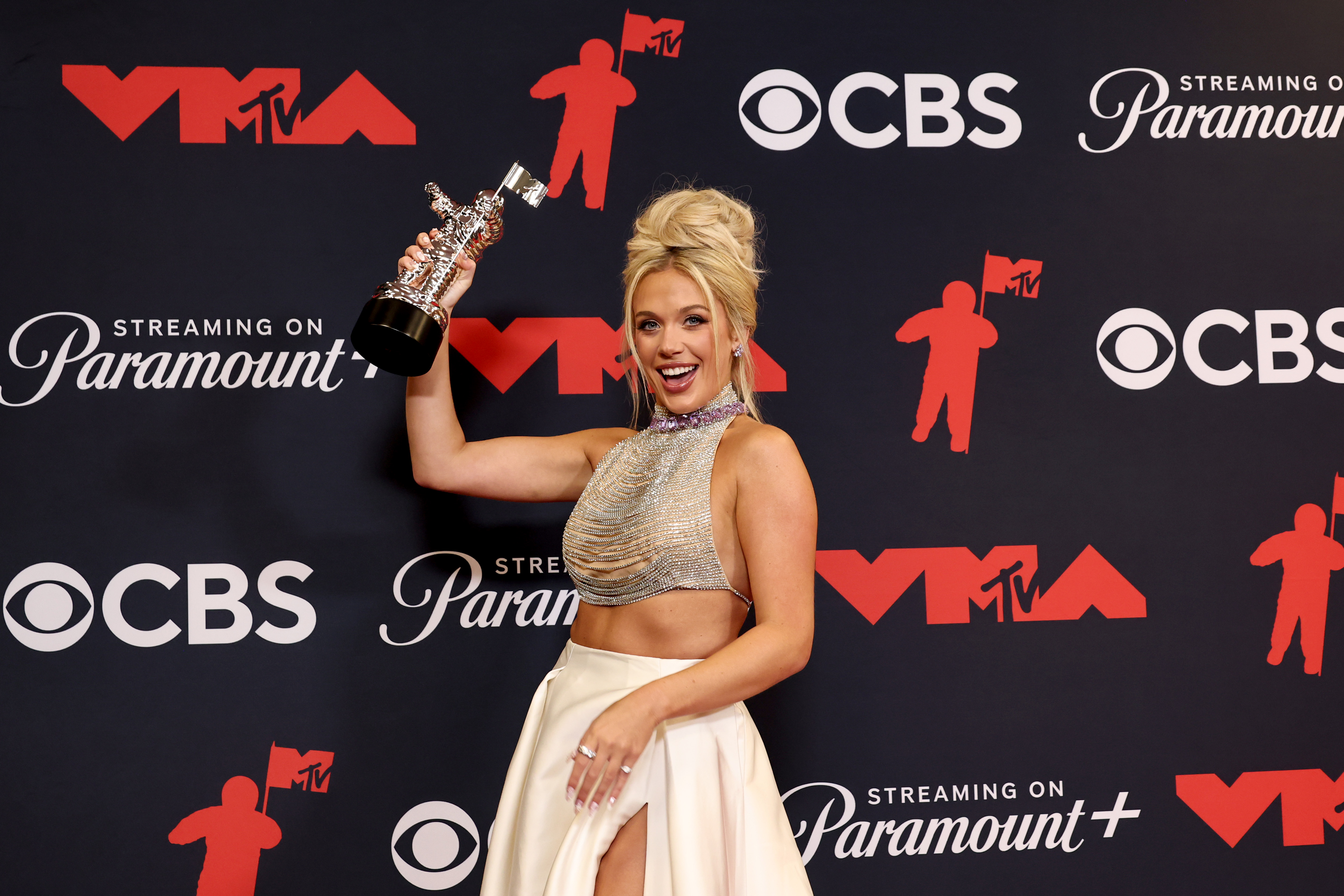 Megan Moroney poses with her Moon Person trophy after winning Best Country at the music awards, celebrating her milestone victory with joy.