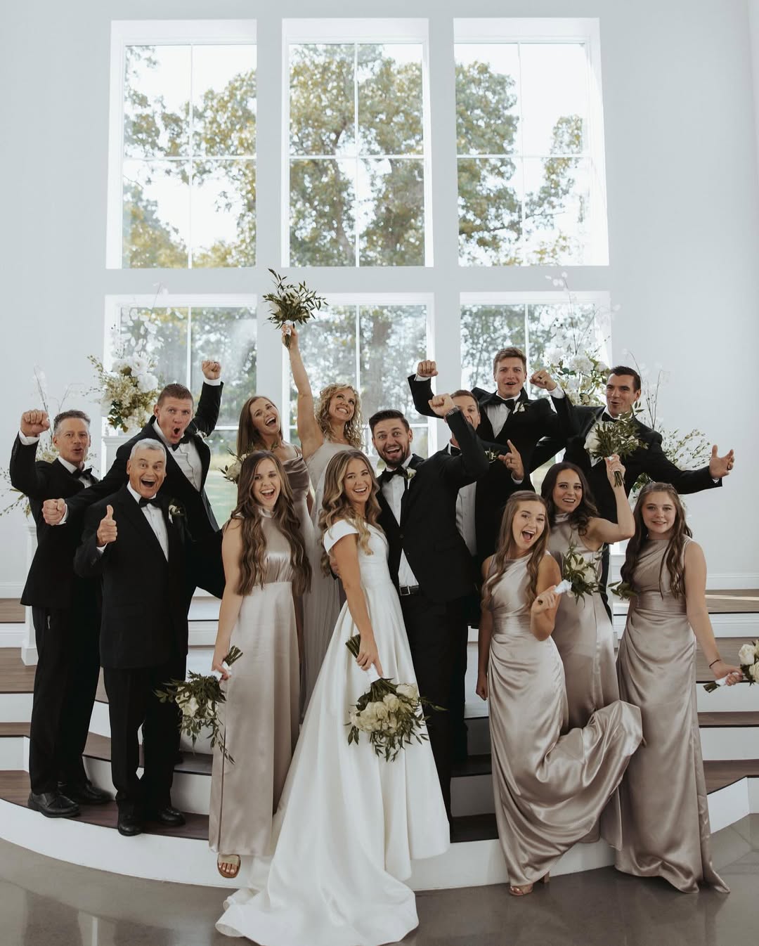 Jana Duggar and Stephen Wissmann pose with their bridal party, everyone cheering and celebrating together against the bright chapel backdrop. | Source: Instagram/janamduggar