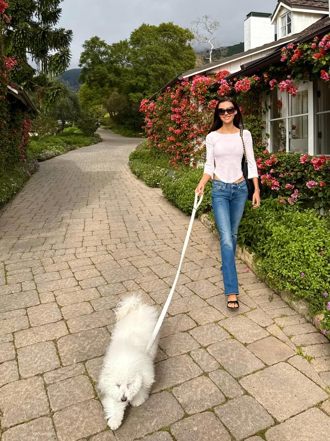 Captured mid-stroll, Nicola walks her dog along a flower-lined stone path, embracing the calm of the outdoors. She smiles at the camera, offering a glimpse into a laid-back day. | Source: Instagram/nicolapeltzbeckham