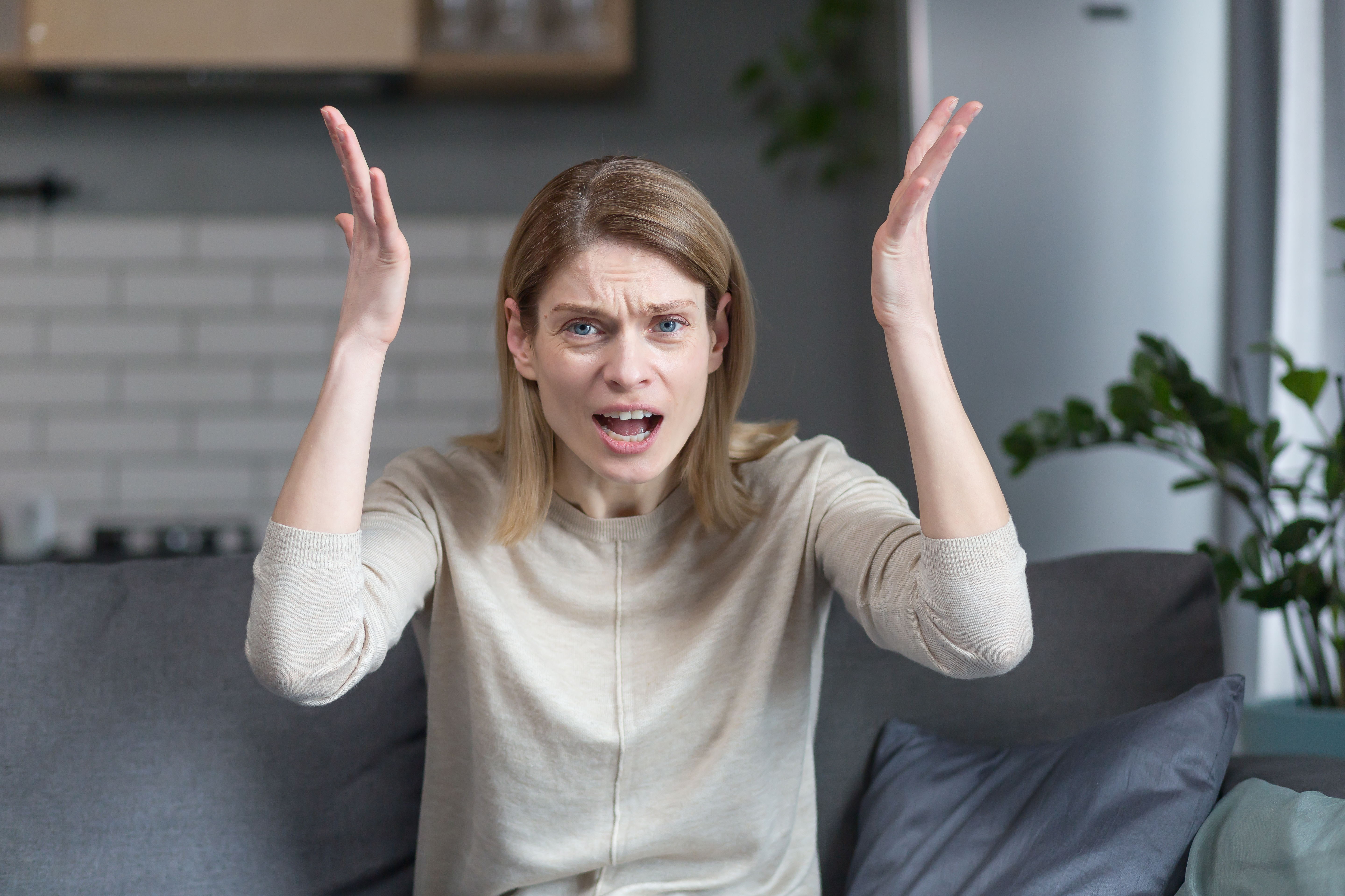 Angry and frustrated woman talking on video call looking at webcam, angrily gesturing with hands while sitting on sofa at home | Source: Getty Images