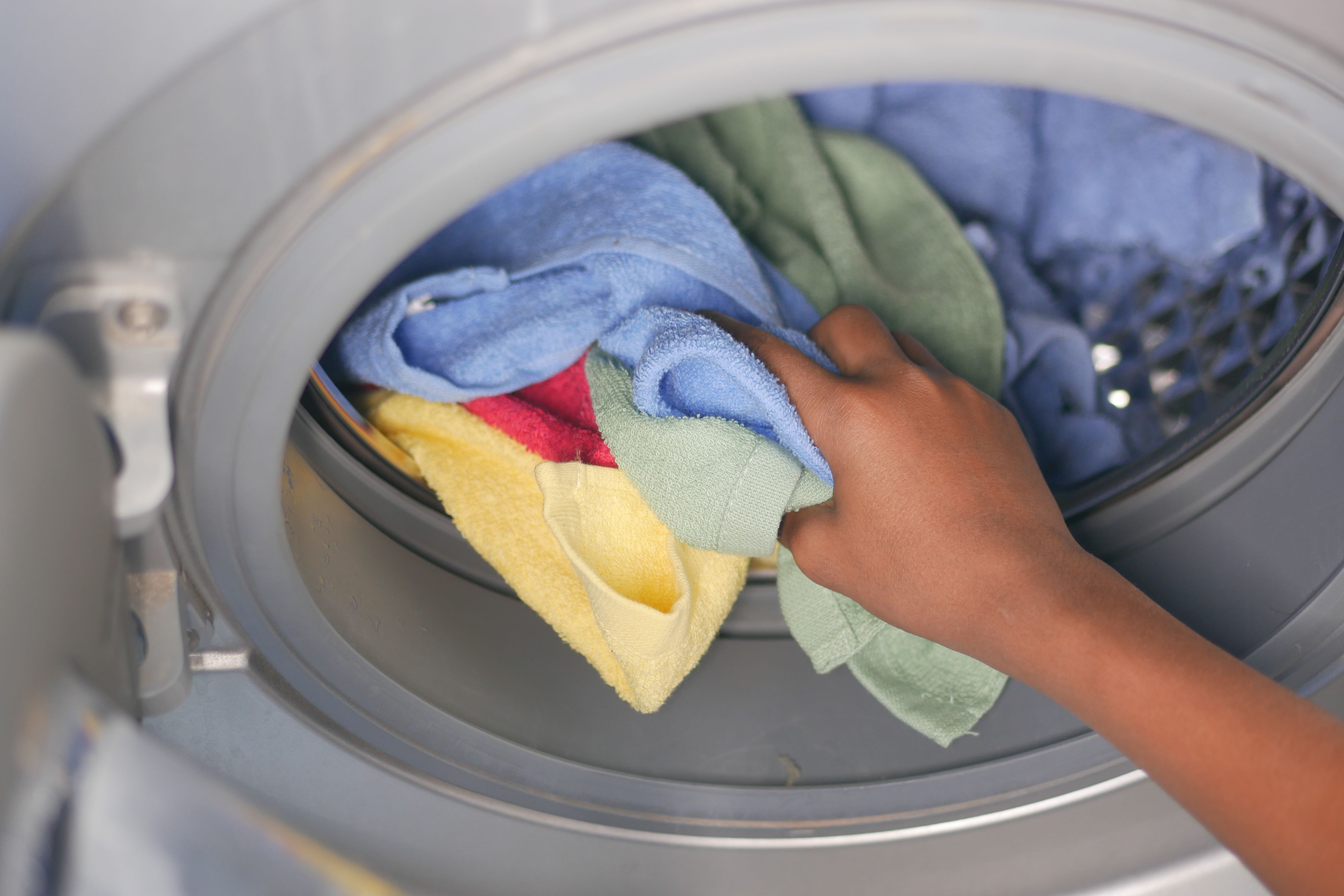 A person placing colorful towels into a washing machine. | Source: Pexels