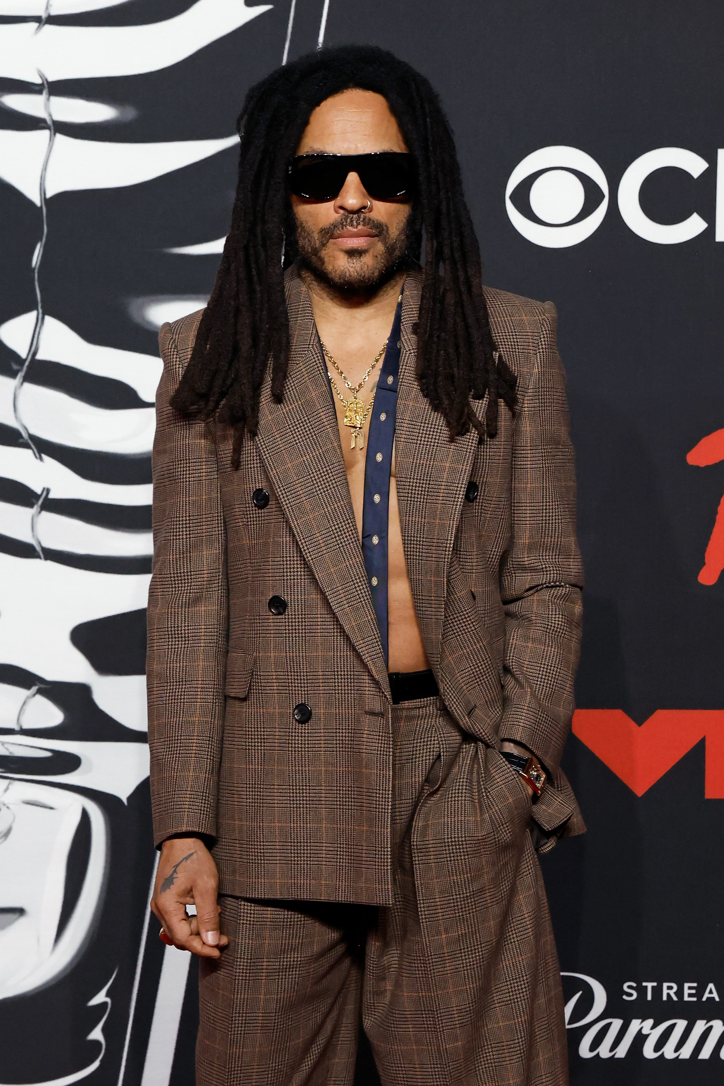 Kravitz, now 61, brought a smoldering sense of style to the 2025 MTV Video Music Awards, stepping onto the red carpet in a sharp brown suit worn without a shirt, layered gold chains, oversized sunglasses, and his signature locs flowing past his shoulders. His look was bold, modern, and effortlessly cool — a testament to how rock star edge can evolve with age without losing its bite.