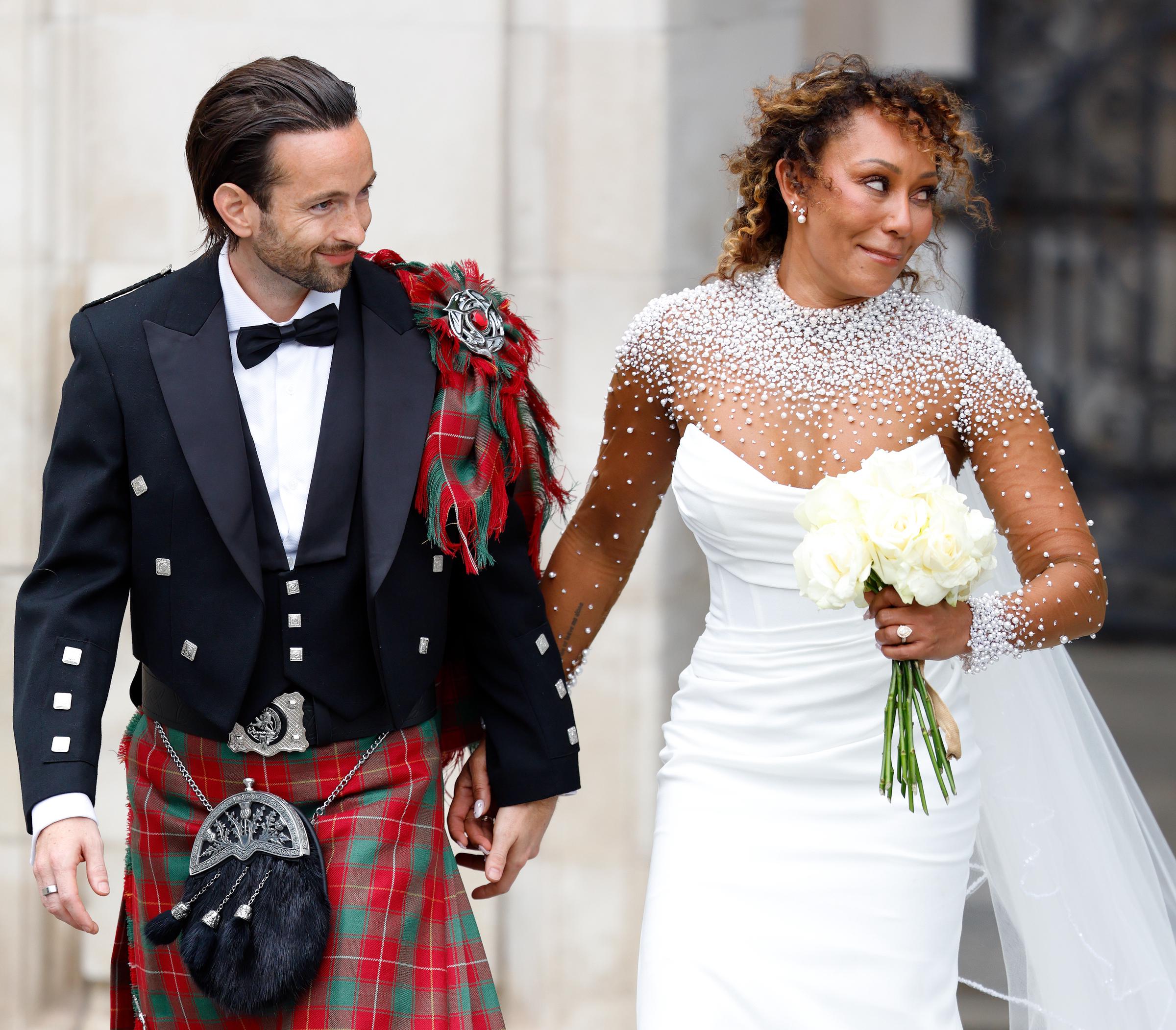 Mel B and Rory McPhee share bright smiles as they walk away together, turning toward the crowd. Their relaxed expressions and easy stride reflect the joy of the occasion, offering a glimpse into the warmth of their celebration.