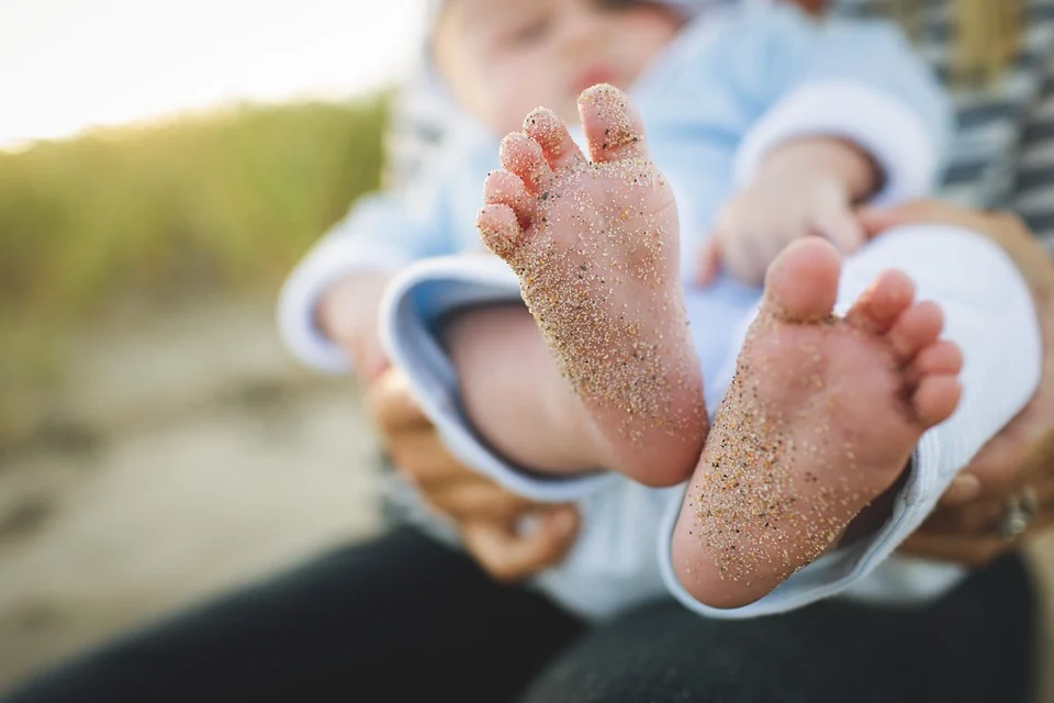 Bebé con los pies llenos de arena en los brazos de un adulto. | Foto: Pixabay