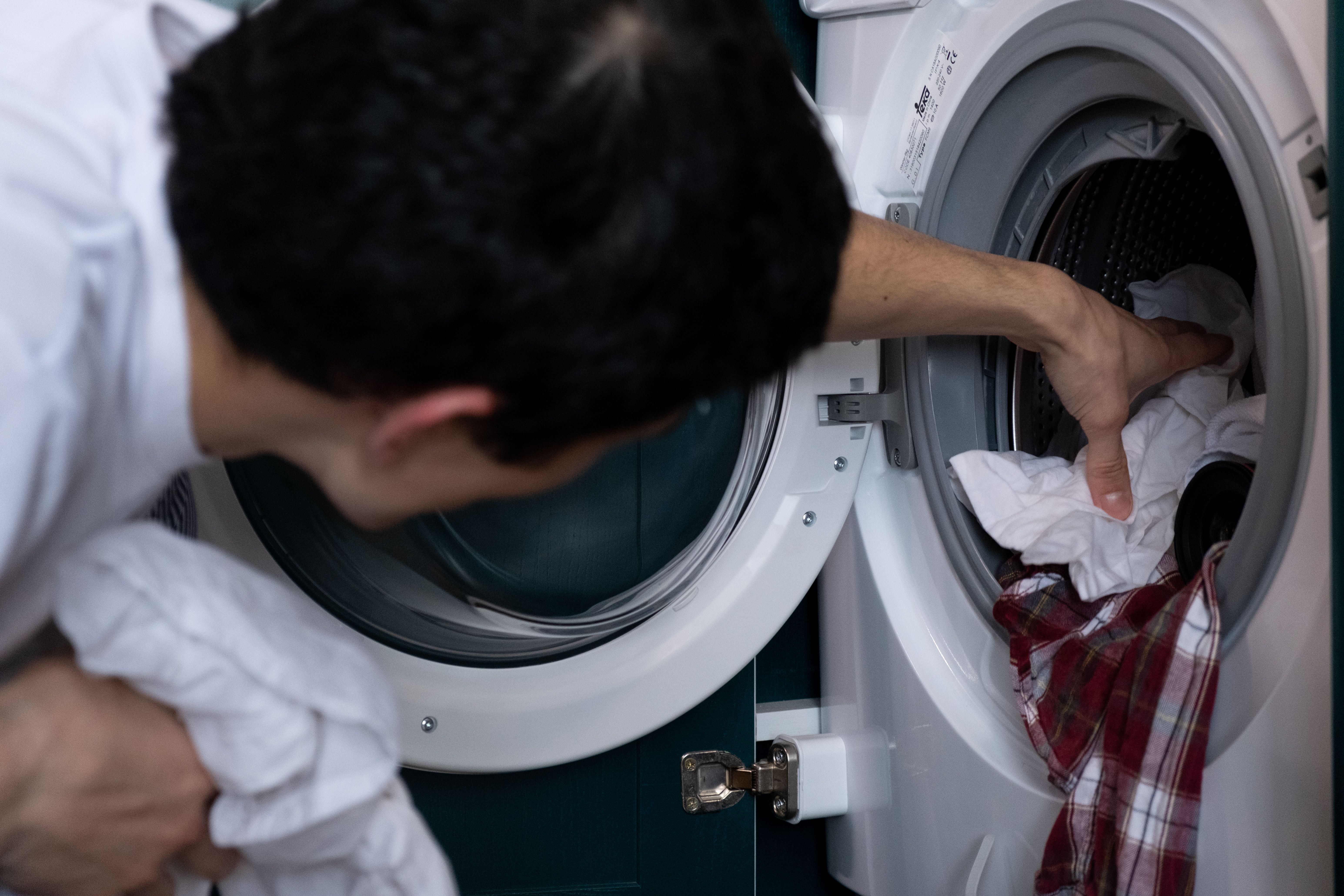 A person loading clothes into a front-load washing machine. | Source: Pexels