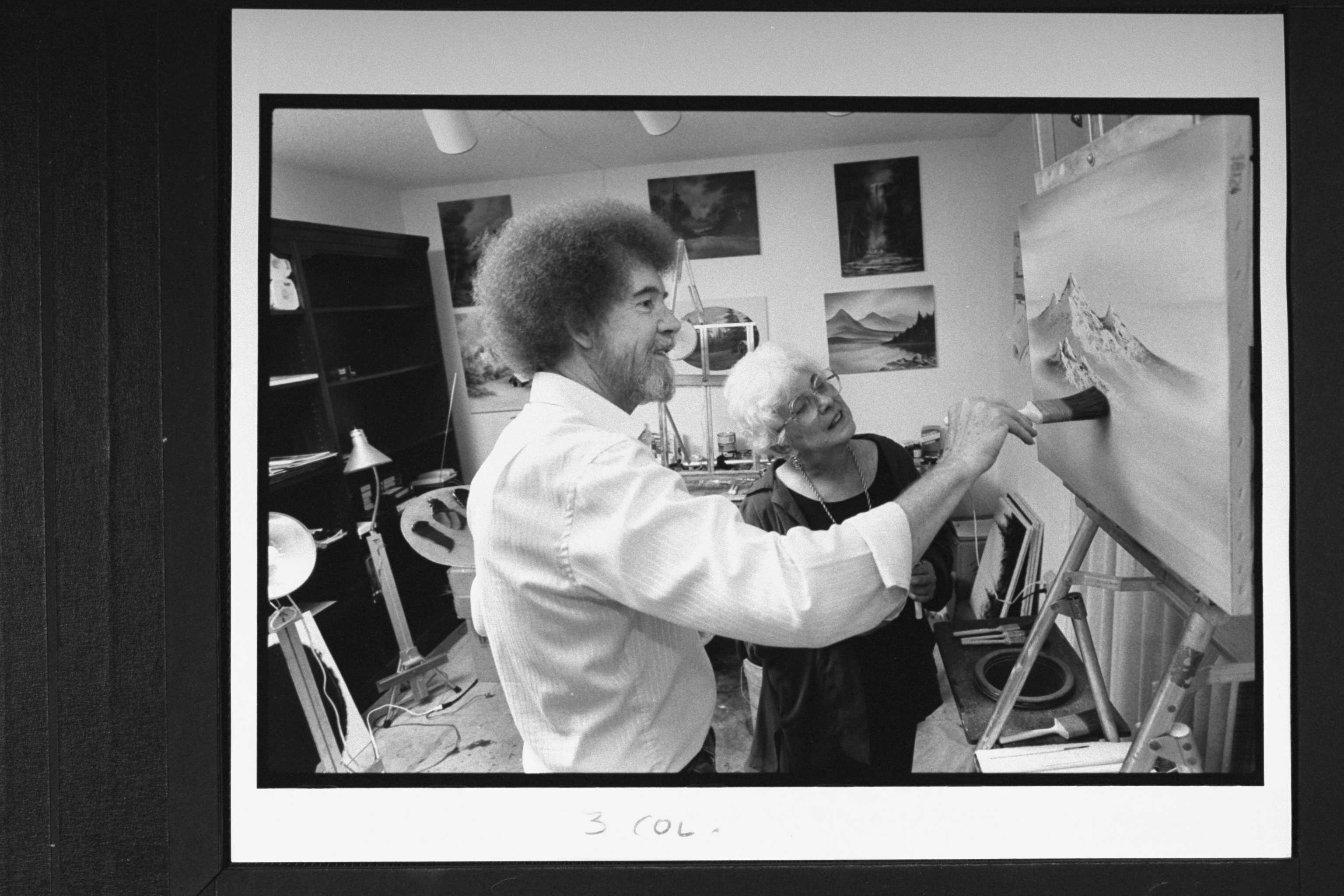 Bob Ross at easel painting one of his mountain landscapes as his business partner Annette Kowalski looks on in his studio at home in 1991. | Source: Getty Images