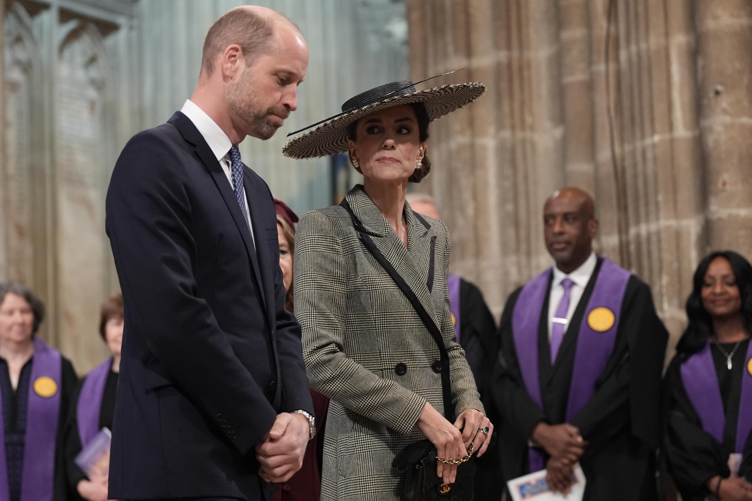 Prince William and the Princess of Wales stand side by side inside the cathedral as the ceremony gets underway, surrounded by clergy and guests in purple robes. The Prince of Wales looks down, while the Princess glances sideways with a measured expression, her black Chanel handbag visible at her side and the boater's single ostrich quill arching above the crowd. Together, the matching check patterns of the coatdress and the hat's houndstooth weave are visible in the same frame.