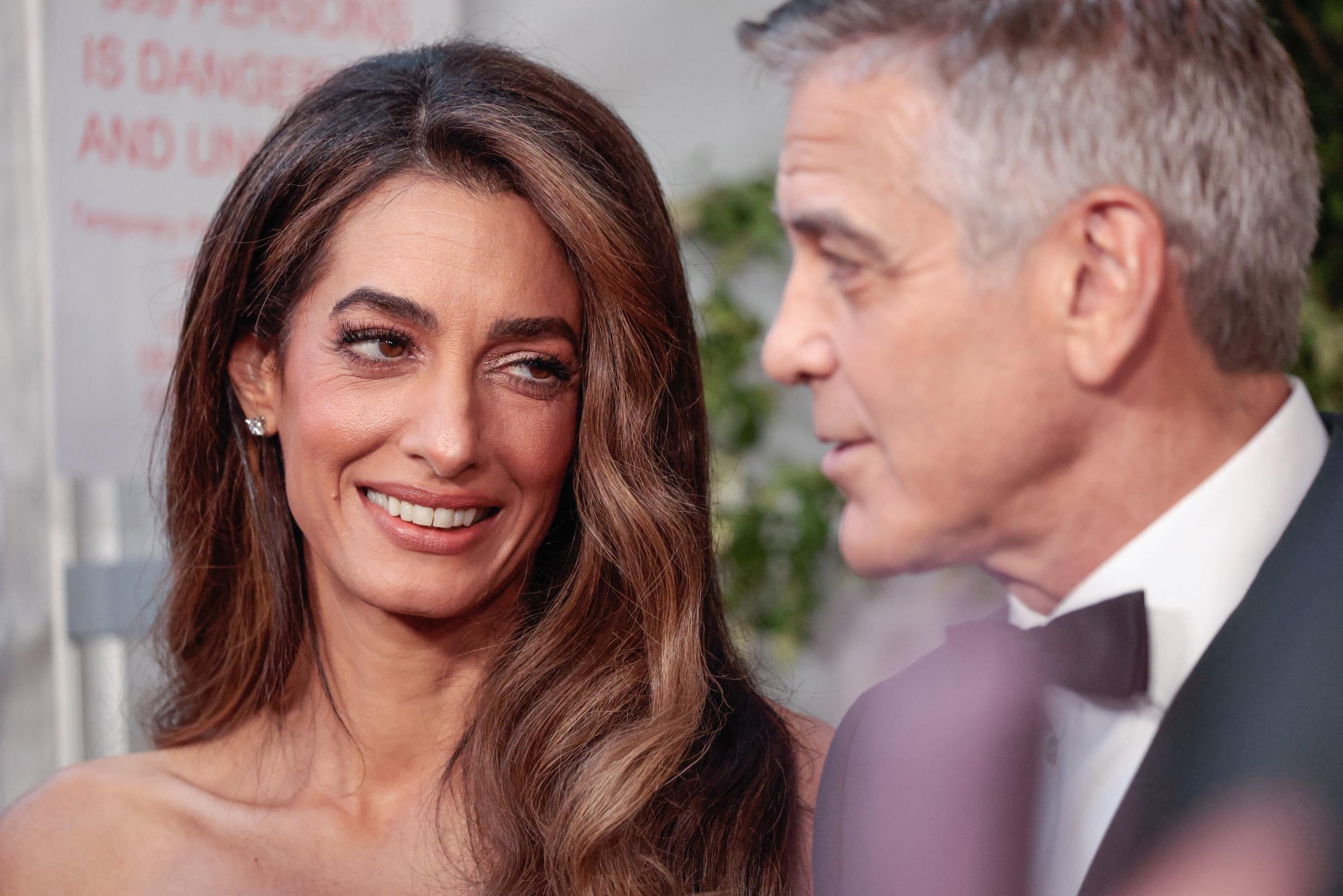 Amal Clooney looks at George with a soft smile, her expression warm and relaxed. The close-up captures a quiet moment between the couple on the red carpet.