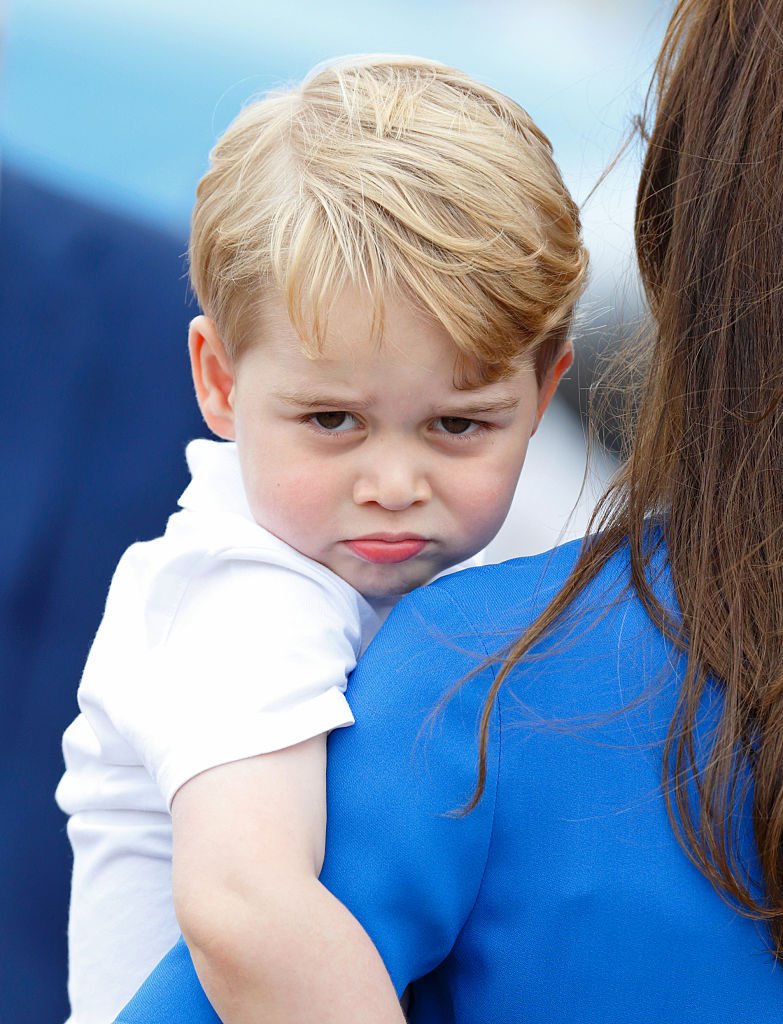 Prince George pouts at the camera while carried by his mother, Kate Middleton. | Source: Getty Images