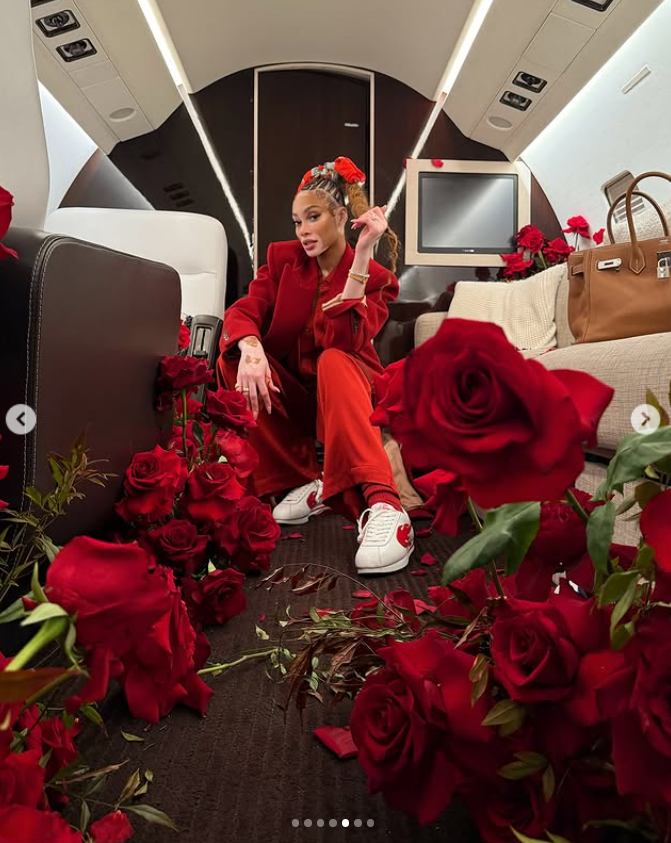 Winnie Harlow poses on the private jet, surrounded by red roses, dressed in a bold red outfit that matches the romantic setting | Source: Instagram/winnieharlow