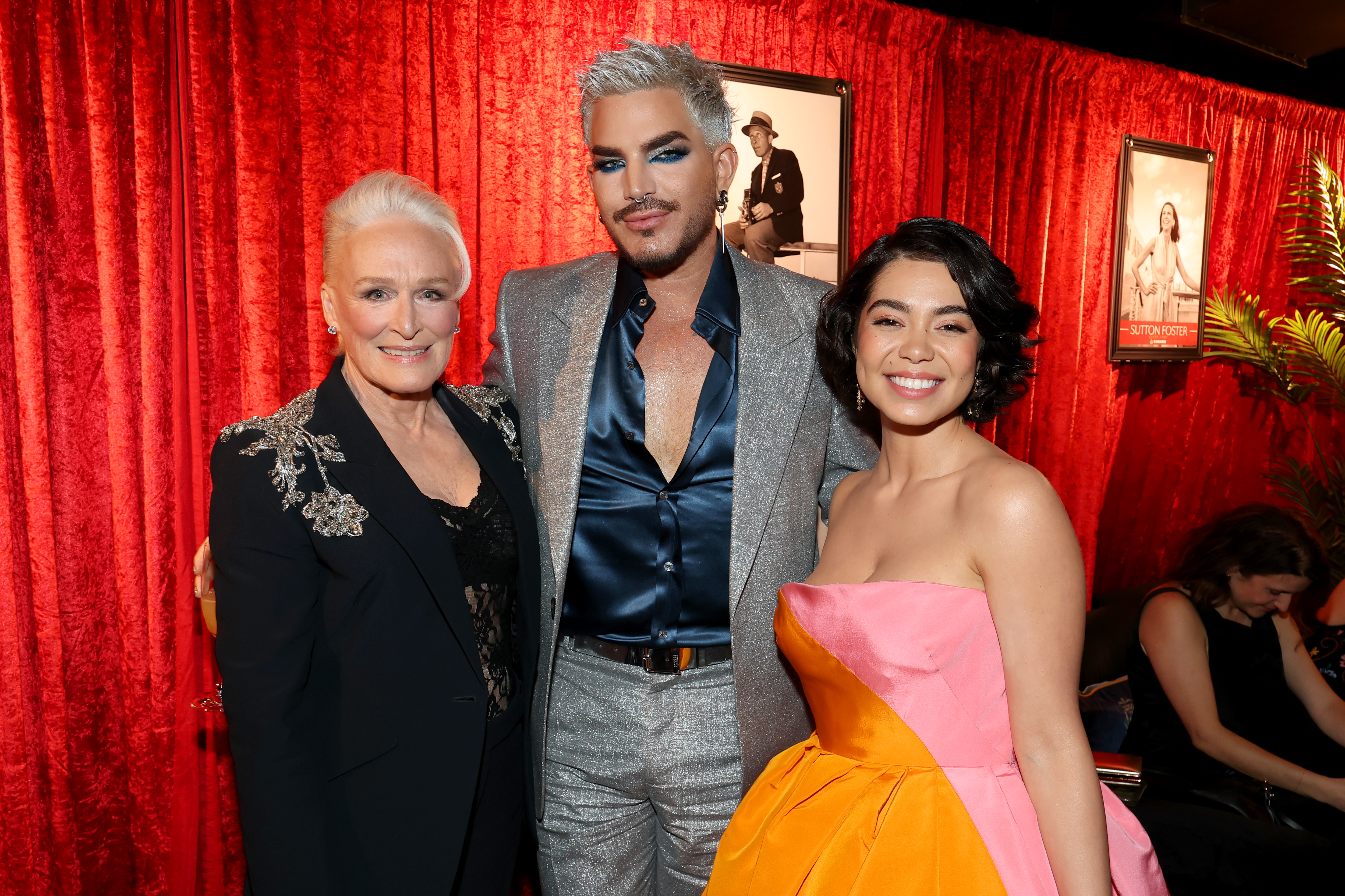 In the green room, Adam Lambert stands between Glenn Close and Auli'i Cravalho. The trio's mix of glamour, sparkle, and vibrant color, paired with relaxed smiles, makes for a memorable, behind-the-scenes moment among stars.