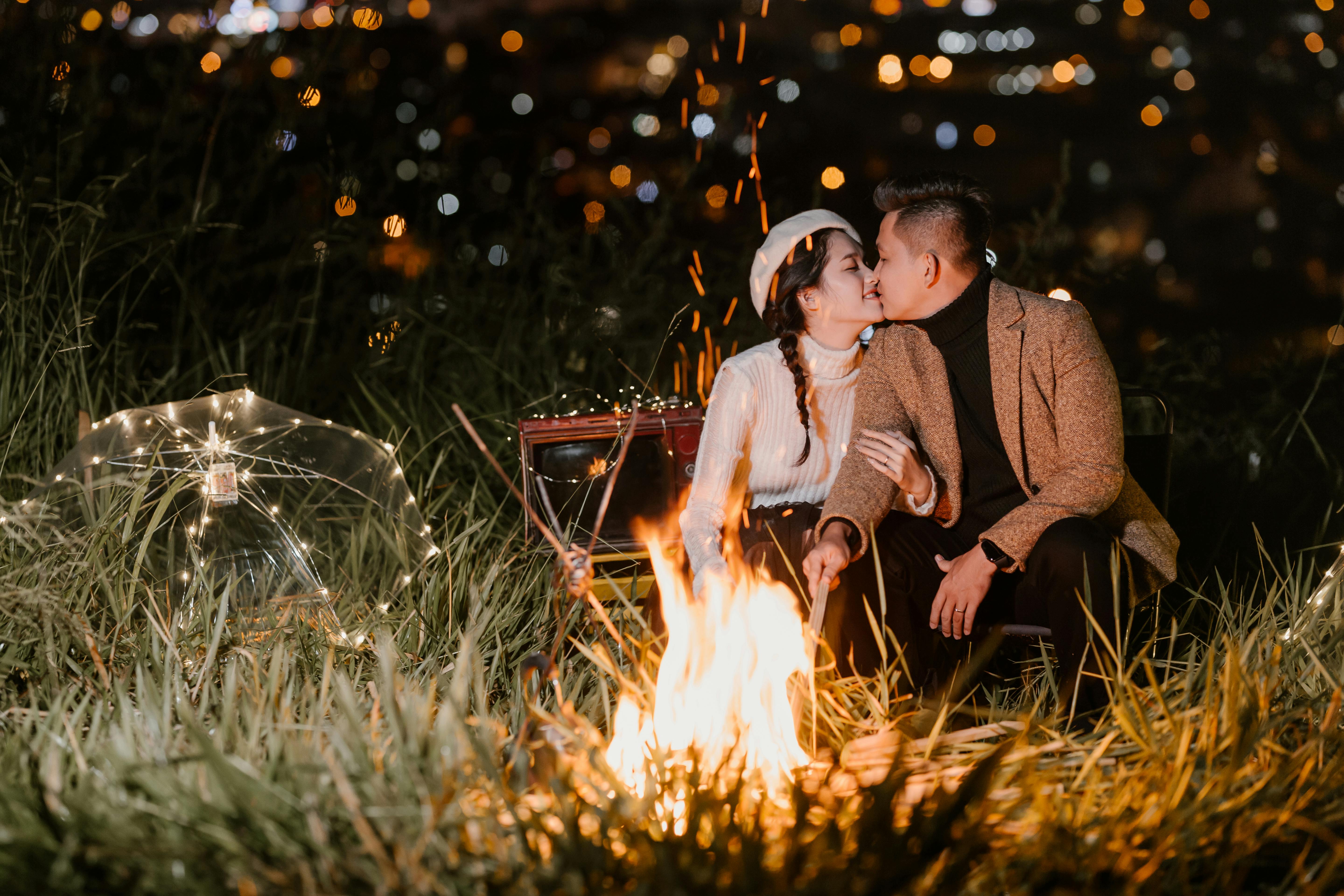 A couple kissing under the moonlight with a fire burning | Source: Pexels