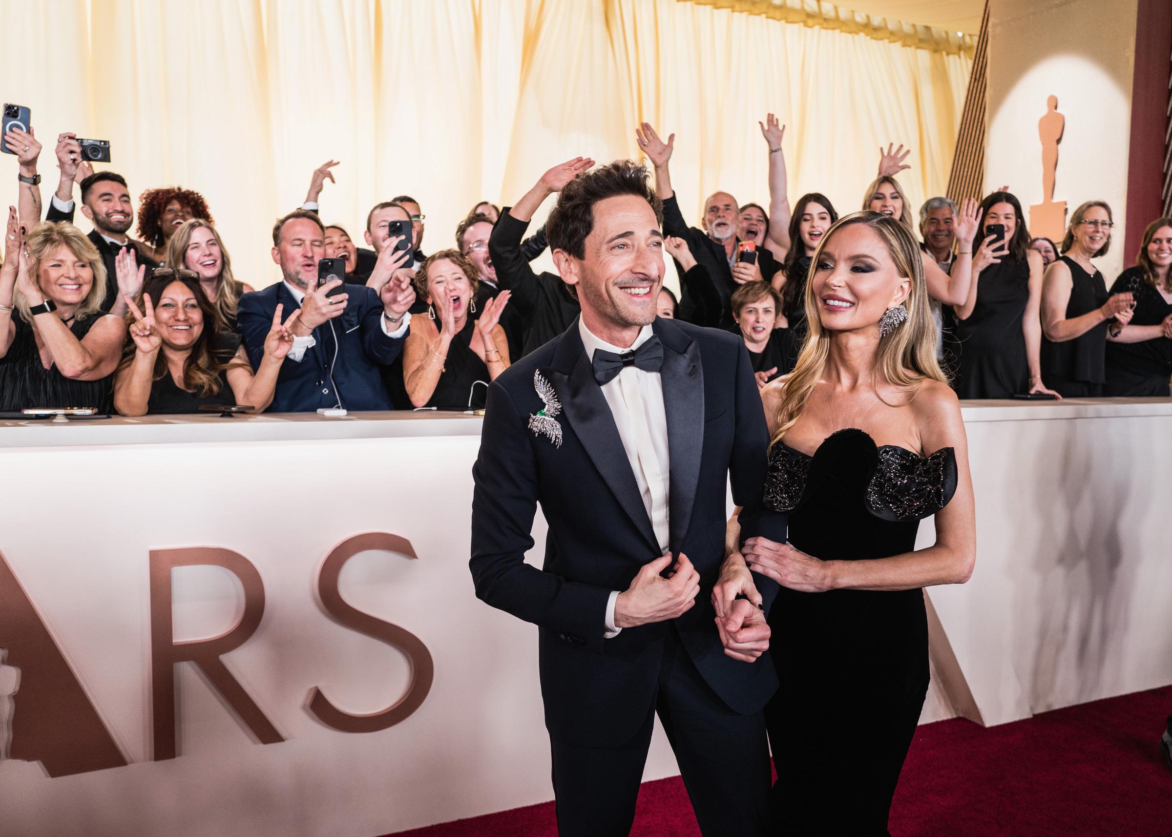 Adrien Brody and Georgina Chapman smiling as the crowd behind them cheers during the 2025 Oscars. | Source: Getty Images