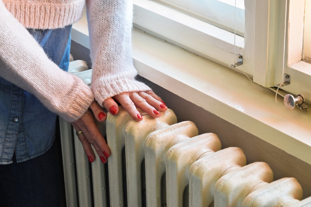 Personas calentando sus manos frente al radiador. | Foto: Shutterstock