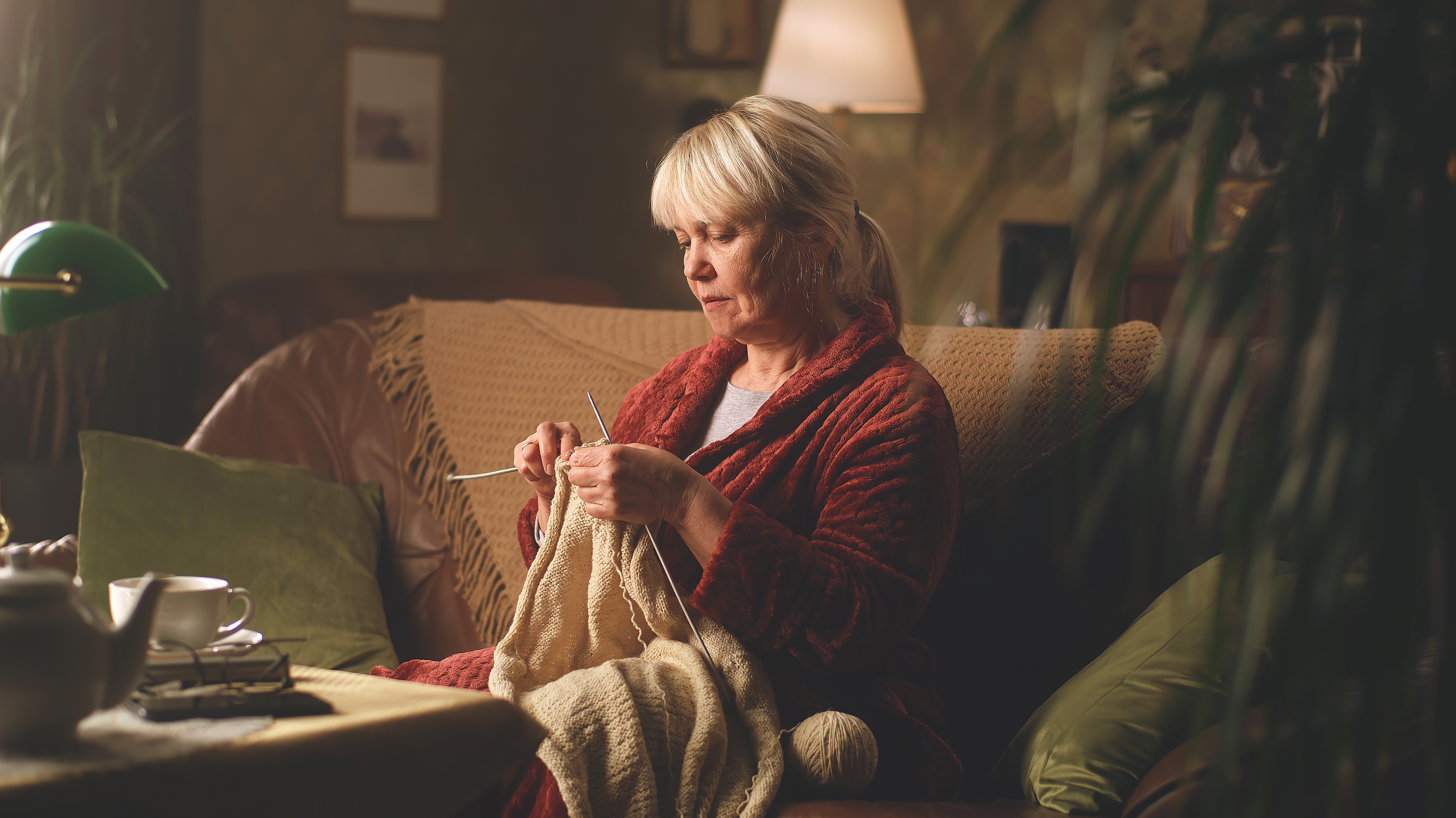 A senior woman knitting a sweater while sitting on the sofa | Source: Shutterstock