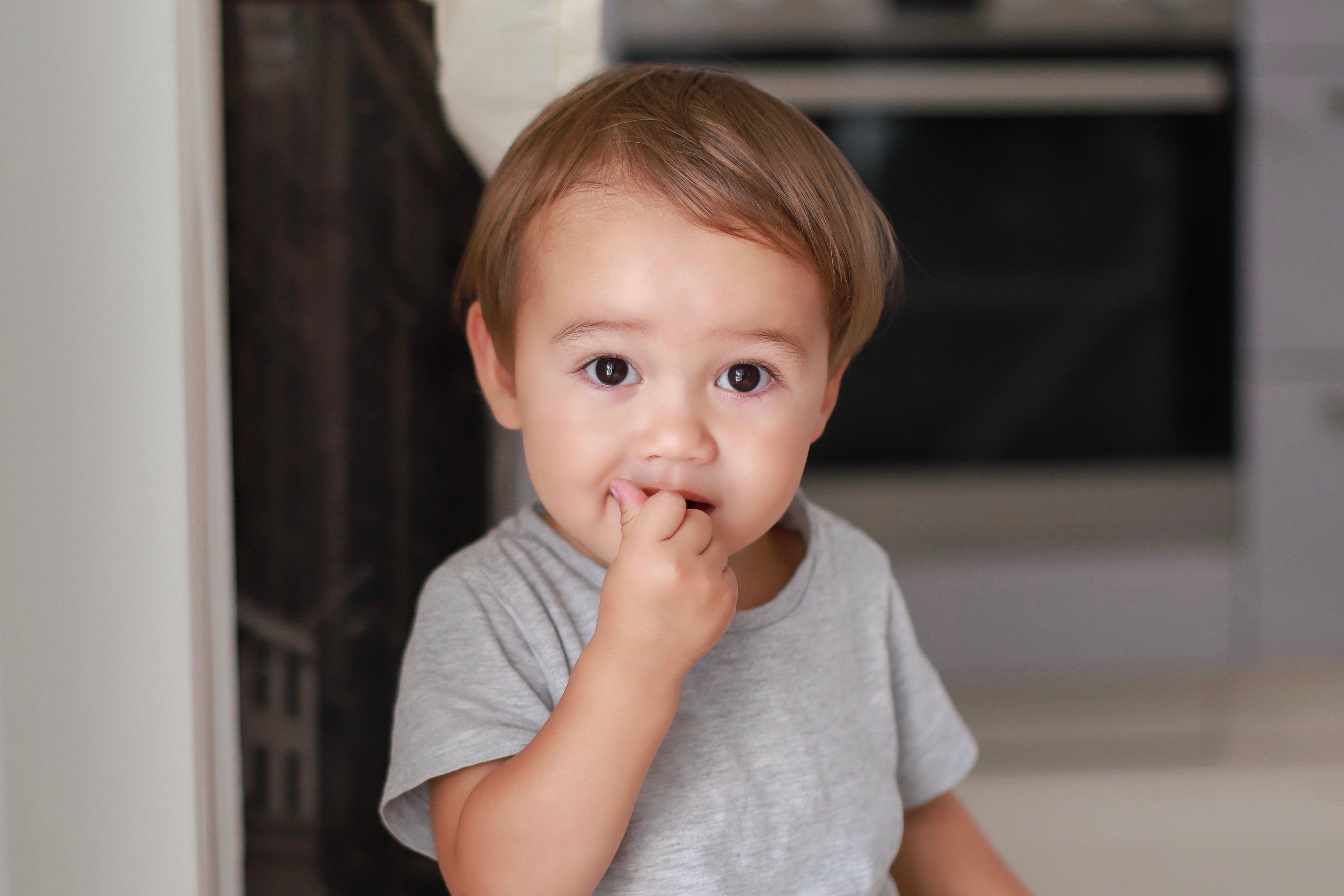 Headshot of baby boy with finger in his mouth eating snack at home. | Source: Shutterstock