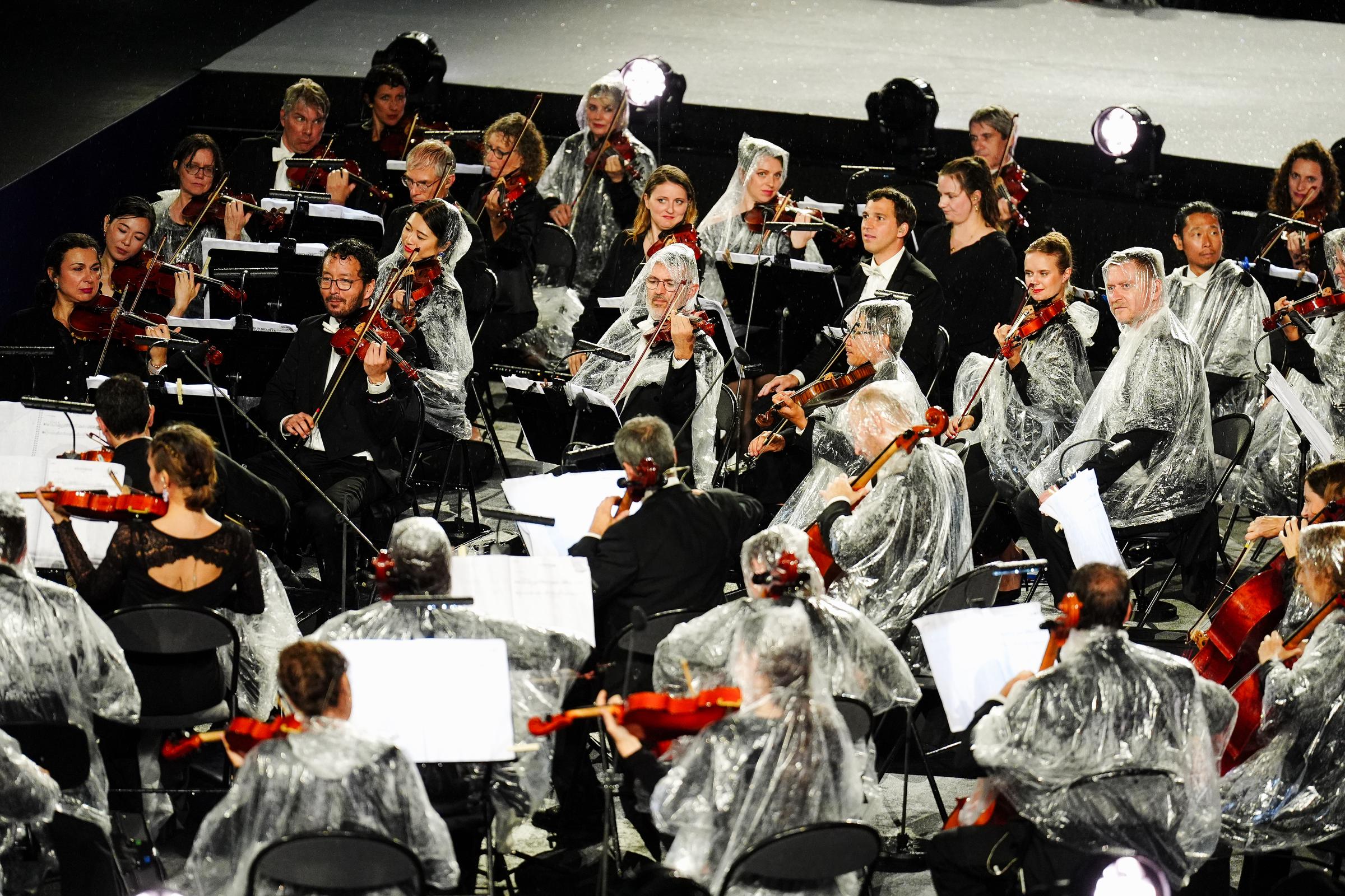 Musicians from the French National Orchestra shelter from the rain during the opening ceremony of the Paris 2024 Olympic Games at the Trocadero in Paris, France, on July 26, 2024. | Source: Getty Images