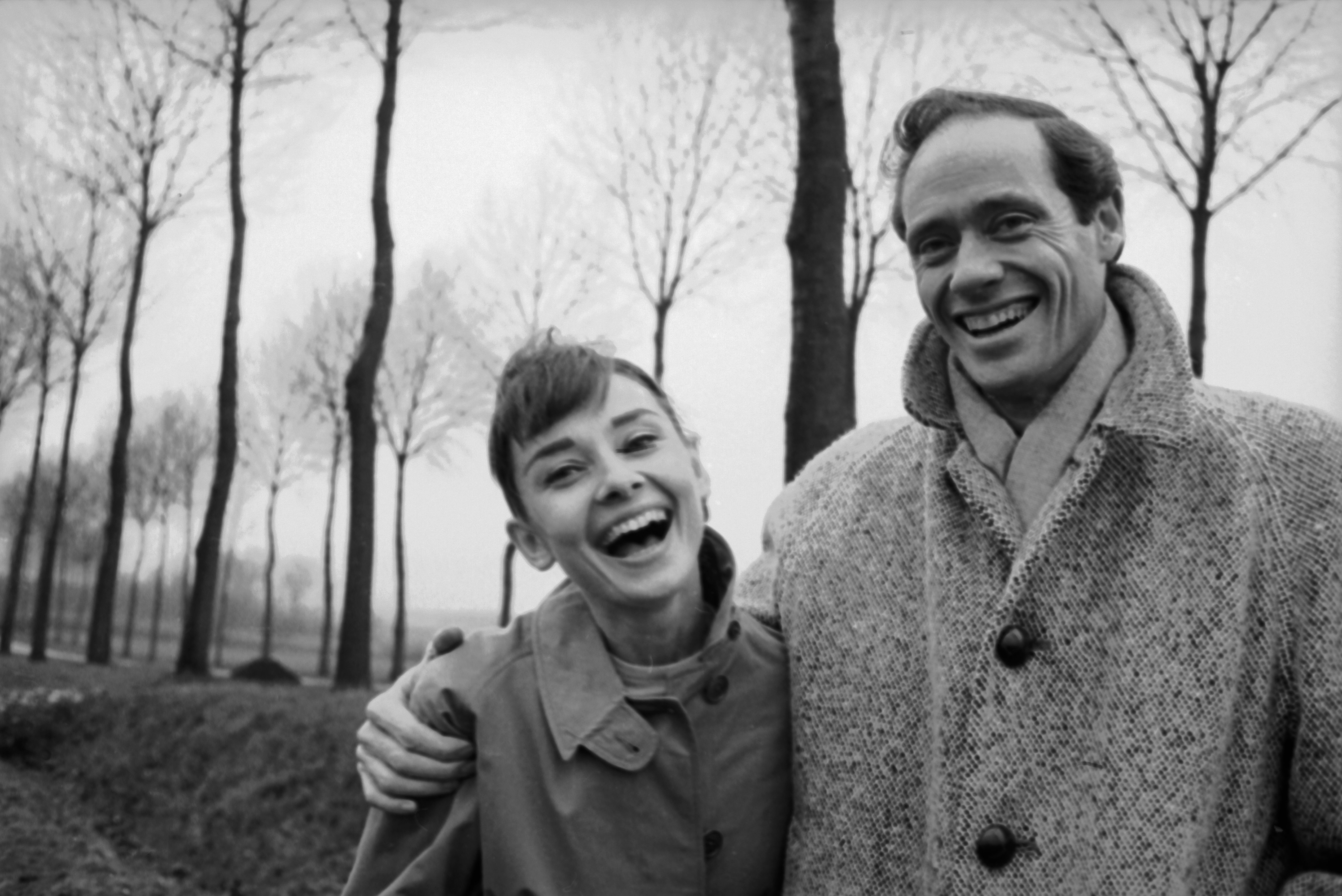 American actor Mel Ferrer (1917 - 2008) buttons up his coat around his wife, actress Audrey Hepburn (1929-1993), on a country road outside Paris, 1956. | Source: Getty Images