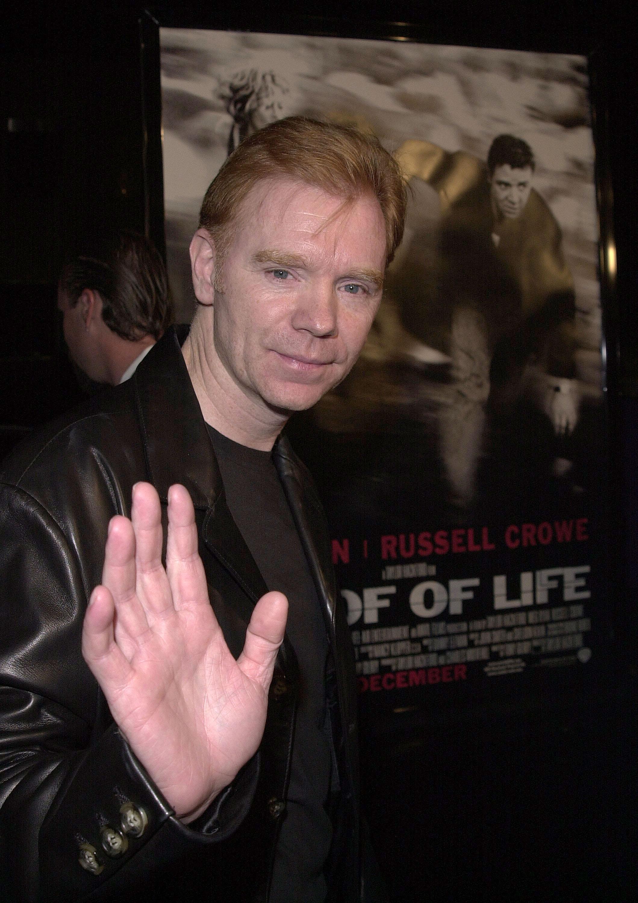 David Caruso raises his hand while arriving at the Beverly Hills premiere of "Proof of Life," standing beside a poster for the Russell Crowe-led film.