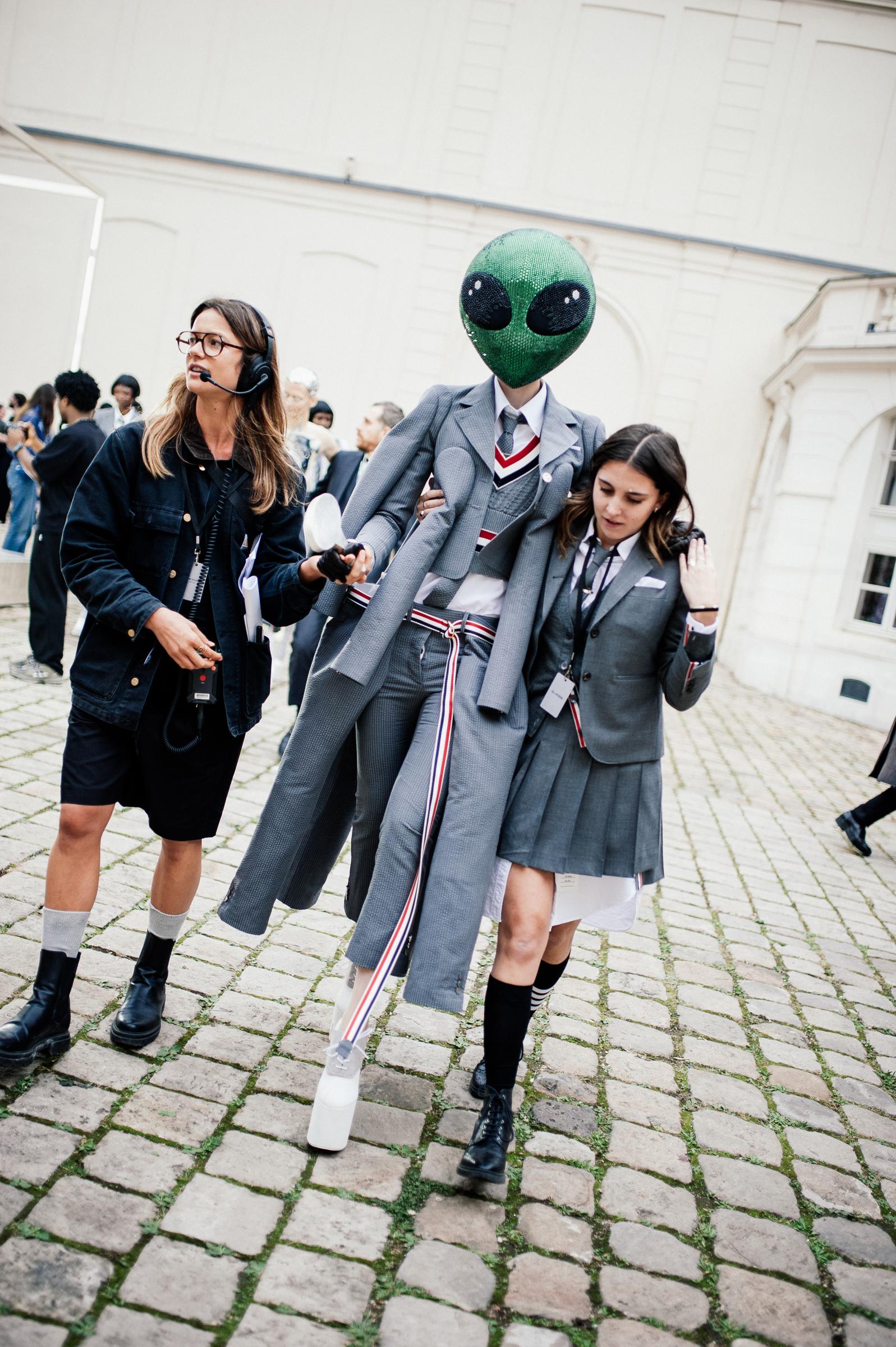 A Thom Browne look is seen backstage during Paris Fashion Week Spring/Summer 2026 in France. The model wears an extraterrestrial green headpiece paired with a classic gray flannel suit. It is transformed with six sleeves and as many legs for a striking, surreal effect.