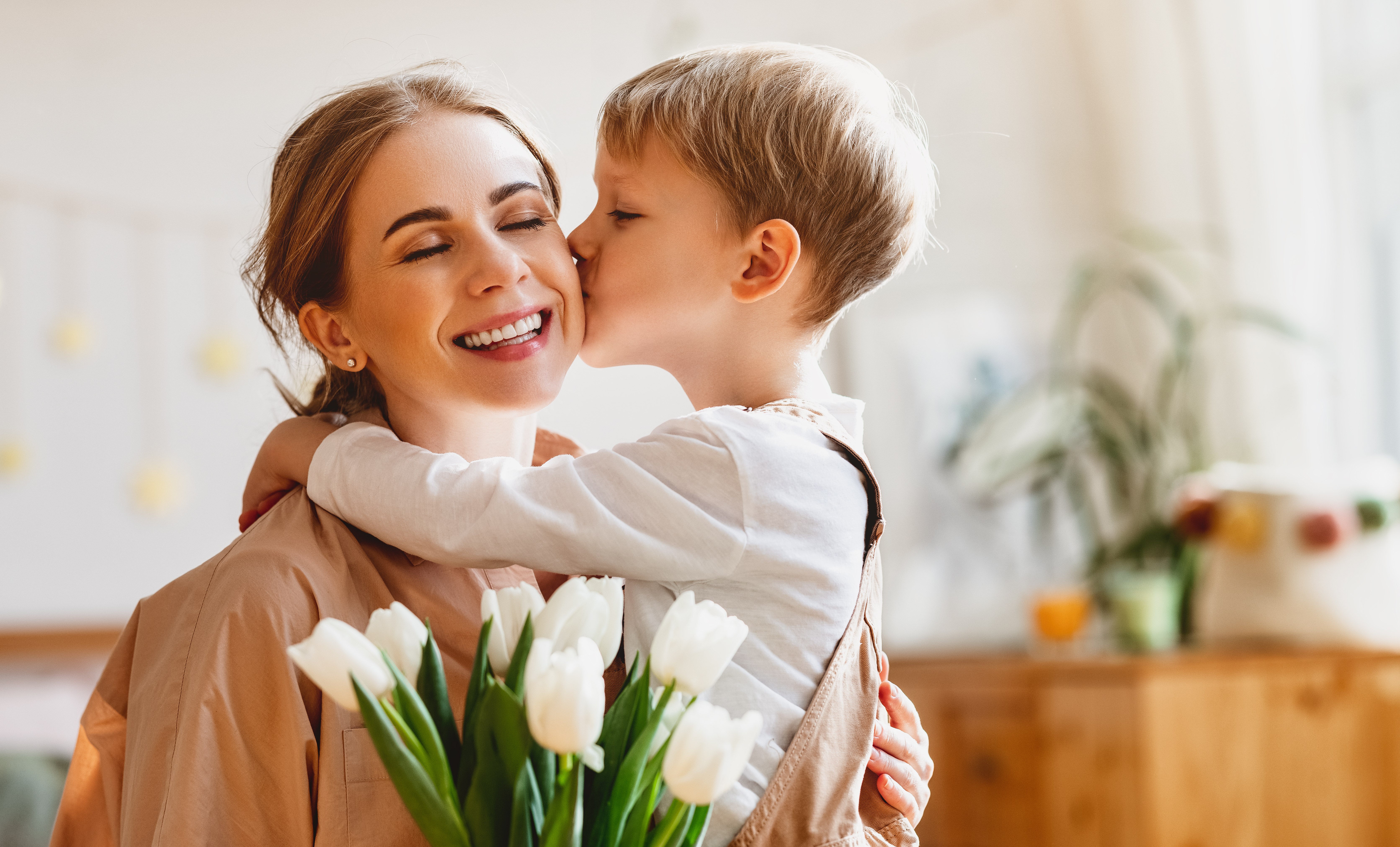 Eine Mutter schließt die Augen, während sie einen Tulpenstrauß in der Hand hält und ihr Sohn sie auf die Wange küsst | Quelle: Shutterstock