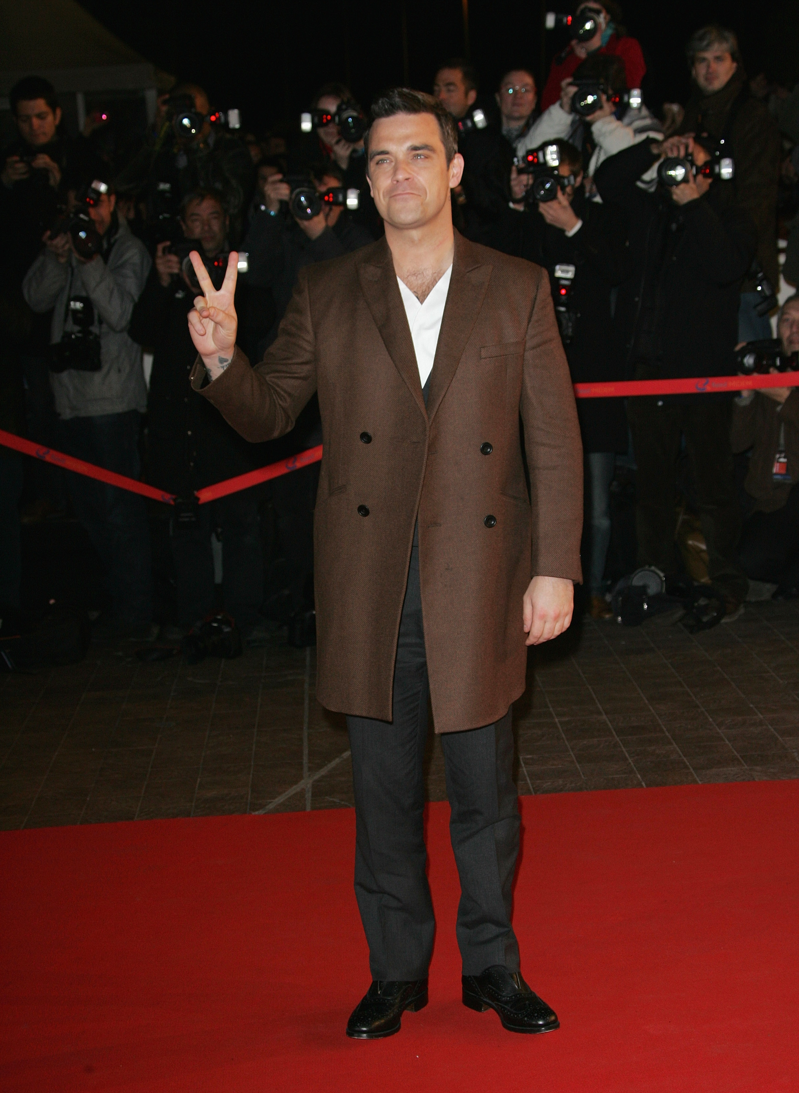 Robbie Williams attended the NRJ Music Awards in Cannes, France, on January 23, 2010. Flashing a peace sign on the red carpet in a sharp brown coat and crisp white shirt, he looked every bit the seasoned star commanding the spotlight.