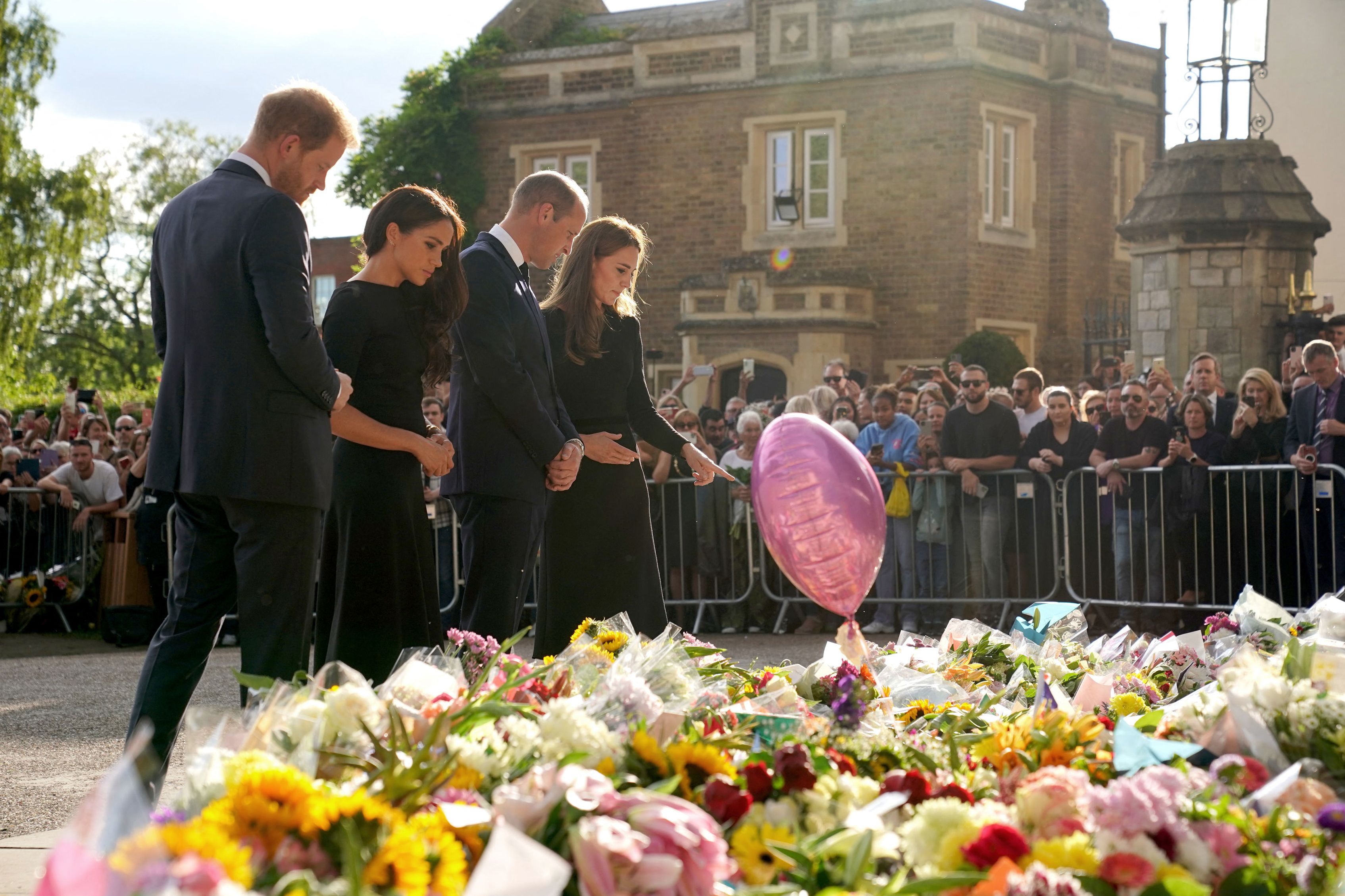 Britain's Prince Harry, Duke of Sussex, his wife Meghan, Duchess of Sussex, Prince William, Prince of Wales and his wife, Catherine, Princess of Wales, look at floral tributes laid by members of the public on the Long Walk at Windsor Castle on September 10, 2022. | Source: Getty Images 
