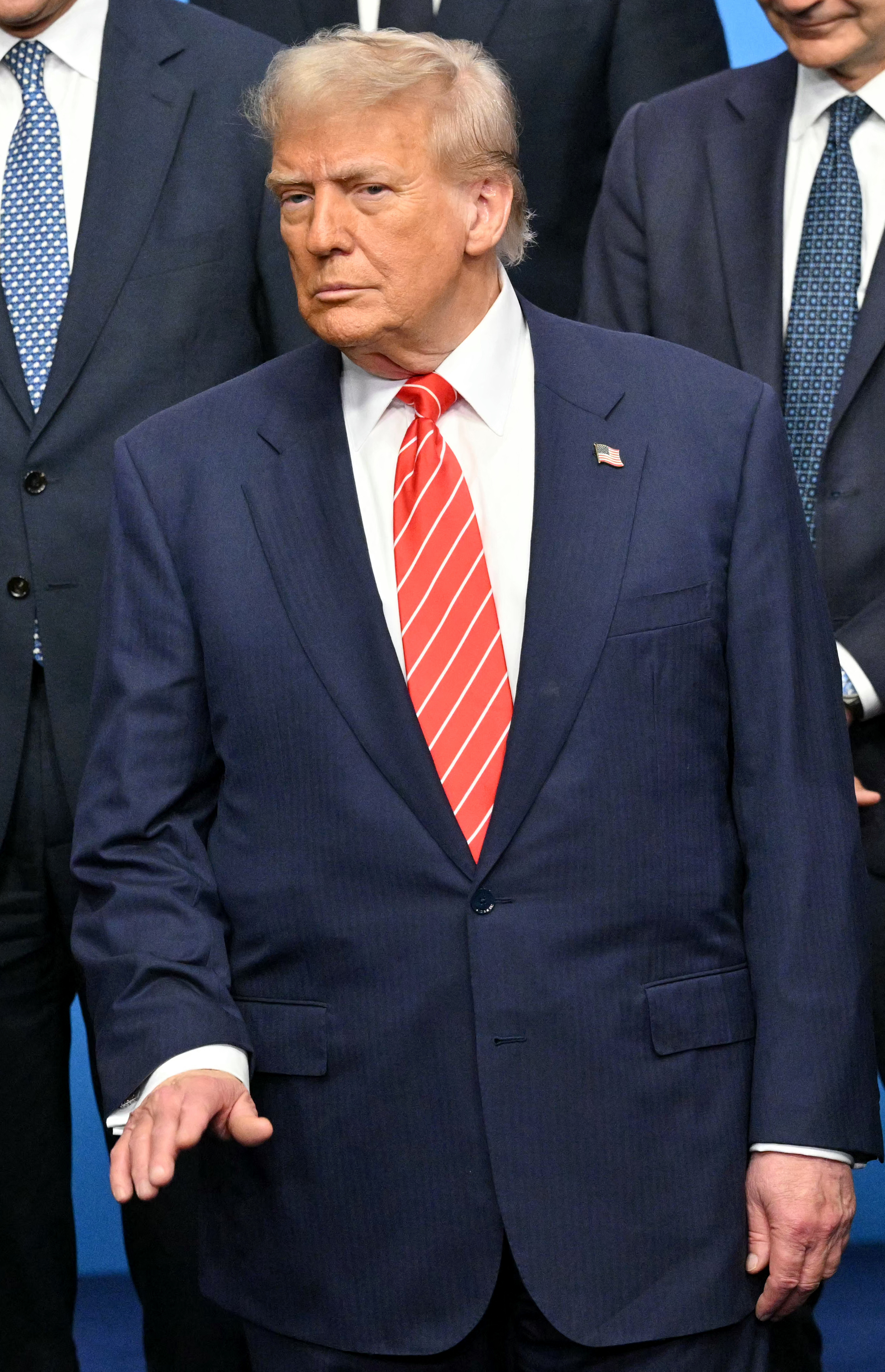 Trump poses with other world leaders at the NATO summit, but the camera’s focus lingers on him. Dressed in a sharp blue suit and a maroon tie with fine white stripes, his posture is composed and expression serious amid the gathering of global power players.
