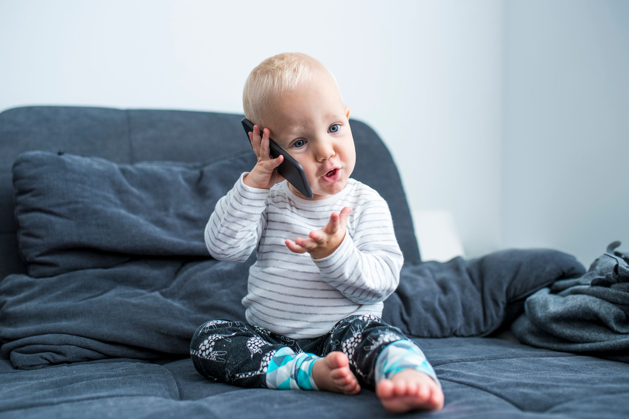 Ein Kleinkind, das sich ein Handy ans Ohr hält. Der Junge sitzt auf einem Sofa. | Quelle: Getty Images