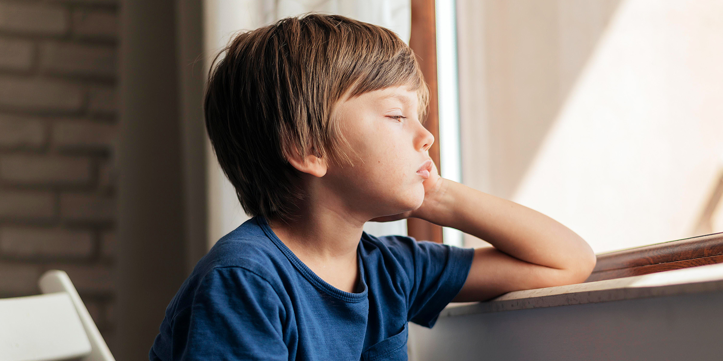 A sad little boy sitting by the window | Source: Freepik