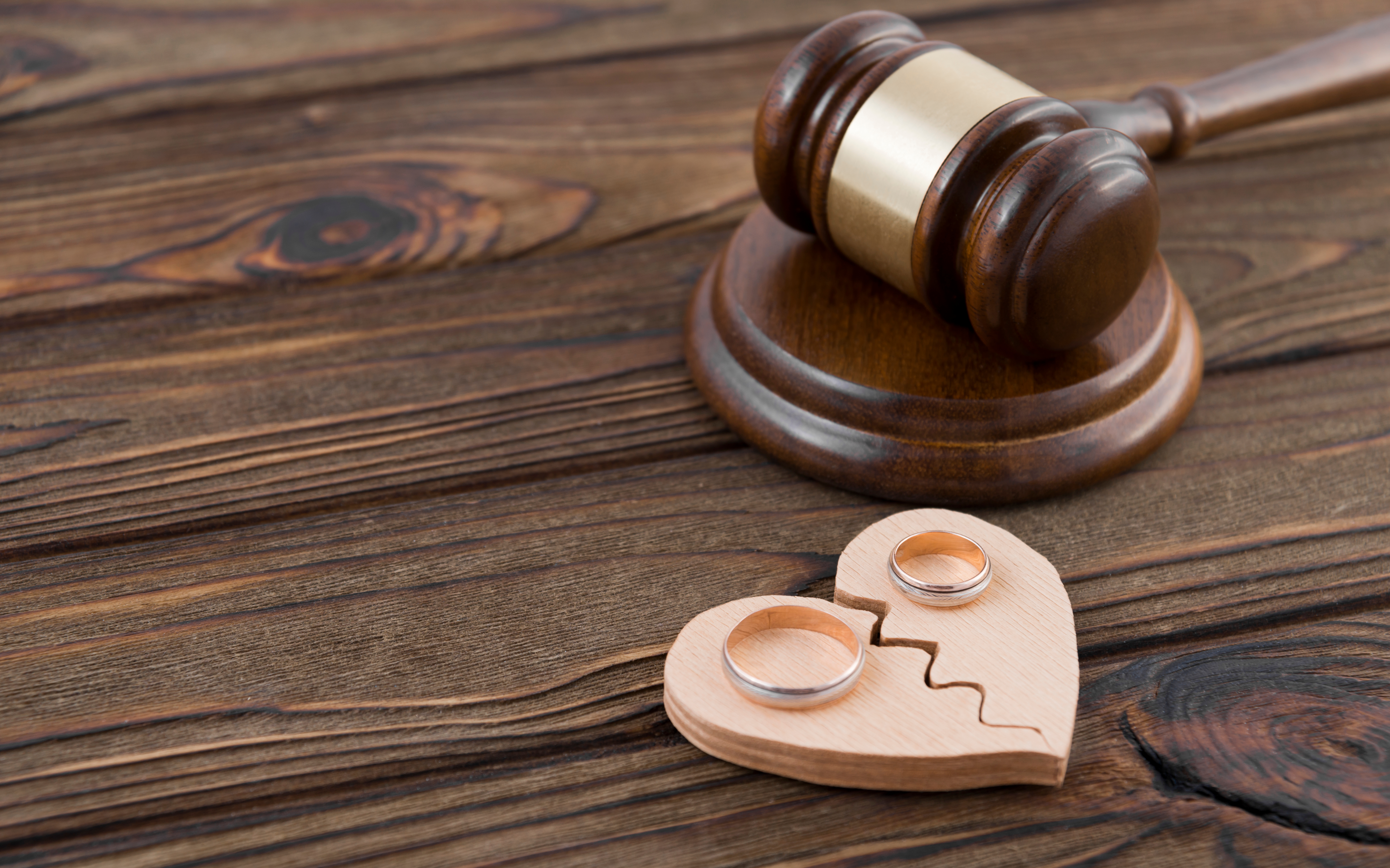 Zwei Eheringe liegen auf einer gebrochenen Herzfigur aus Holz mit einem Richterhammer auf einem hölzernen Hintergrund | Quelle: Shutterstock