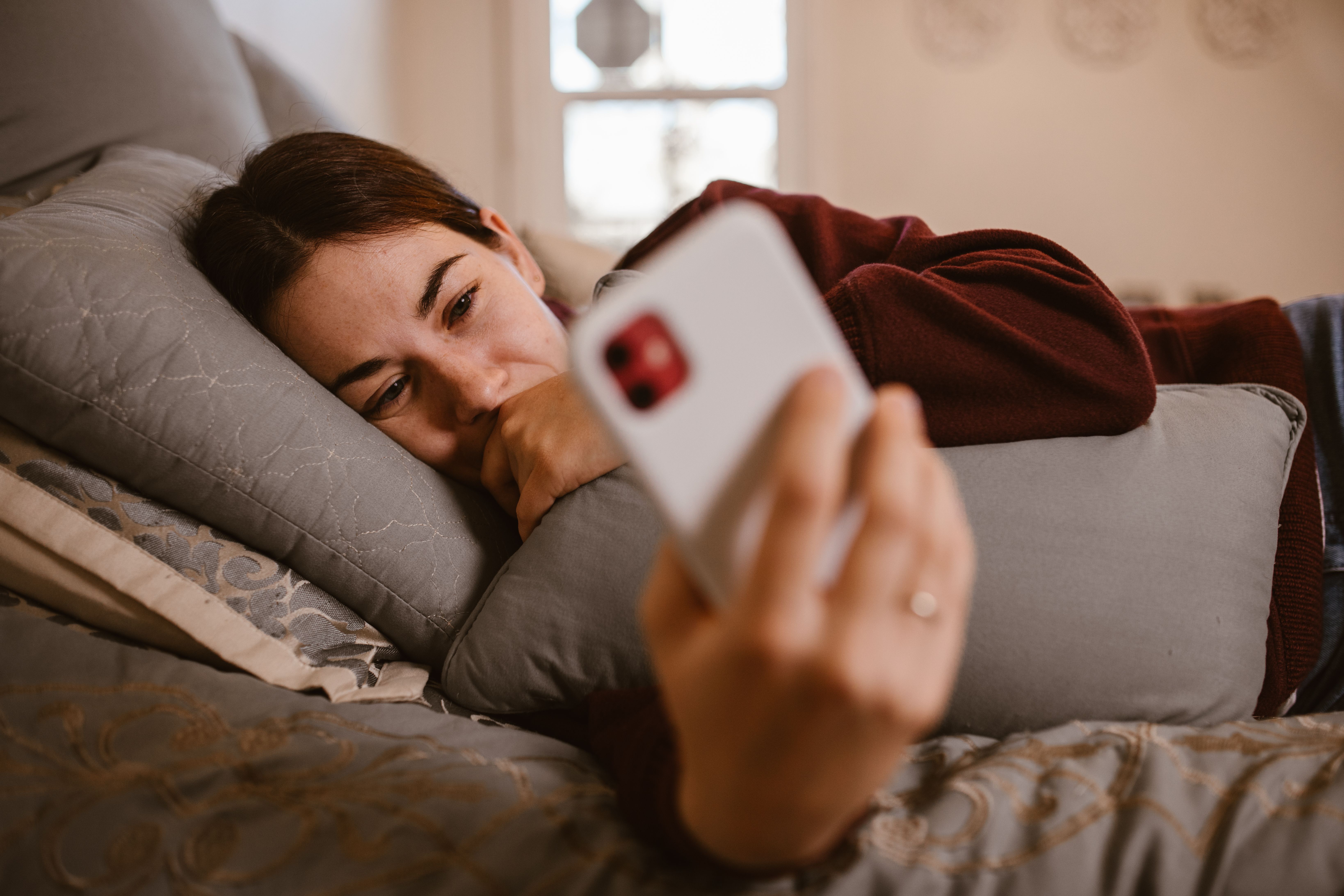 A woman looking at her phone while lying in bed | Source: Pexels