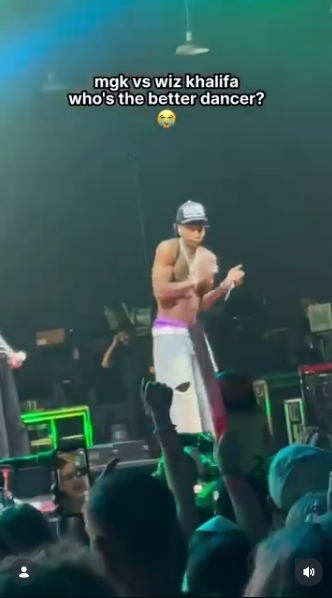 Shirtless and wearing layered chains, Wiz Khalifa performs an energetic sequence as fans cheer from the audience below. The dance battle quickly became one of the most talked-about moments from the Charlotte stop of the tour. | Source: Instagram/mgkmagic