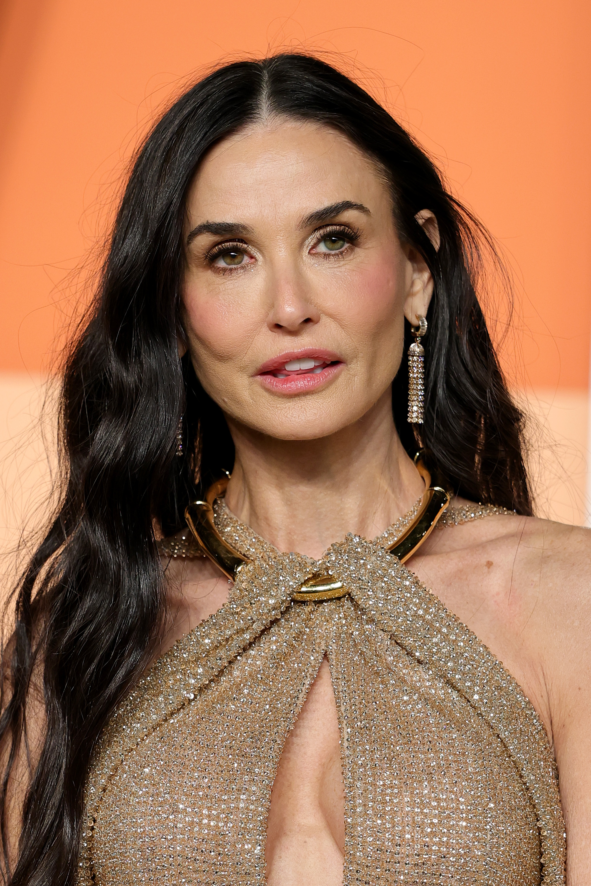 Demi Moore attends the 2025 Vanity Fair Oscar Party hosted by Radhika Jones at the Wallis Annenberg Center for the Performing Arts on March 2, 2025, in Beverly Hills, California. The actress styled her long, dark waves with a center part, pairing the look with a sparkling gold halter gown and statement earrings.